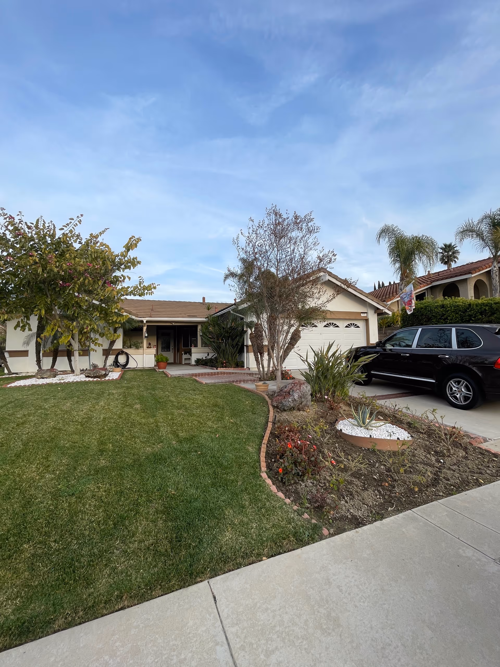 Front view of a single-story senior living home with a lawn, driveway, and garden beds.