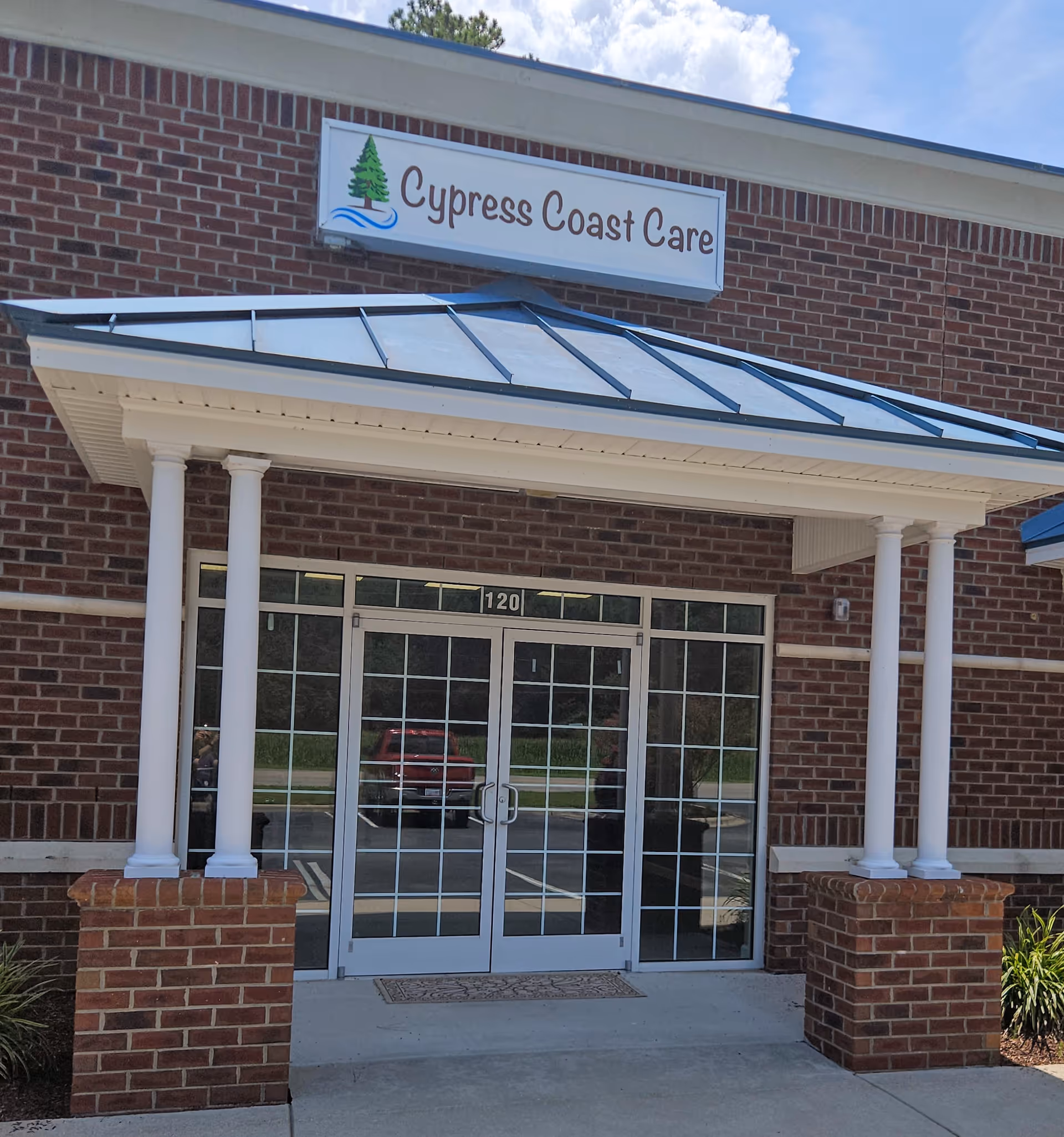 Brick exterior with glass double doors, white columns, and Cypress Coast Care sign above.