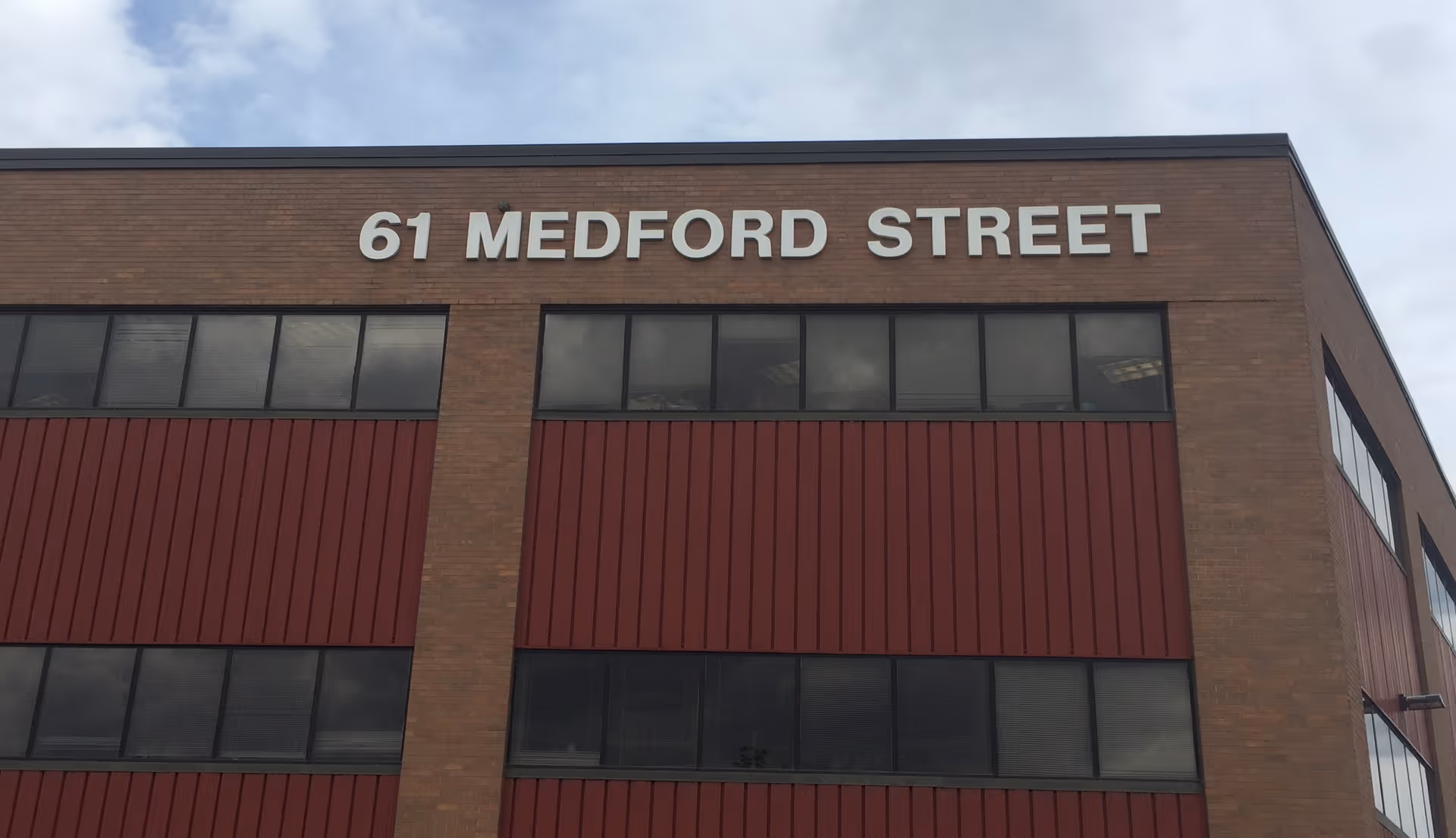 Brick building facade with a large 61 Medford Street sign and red paneling.