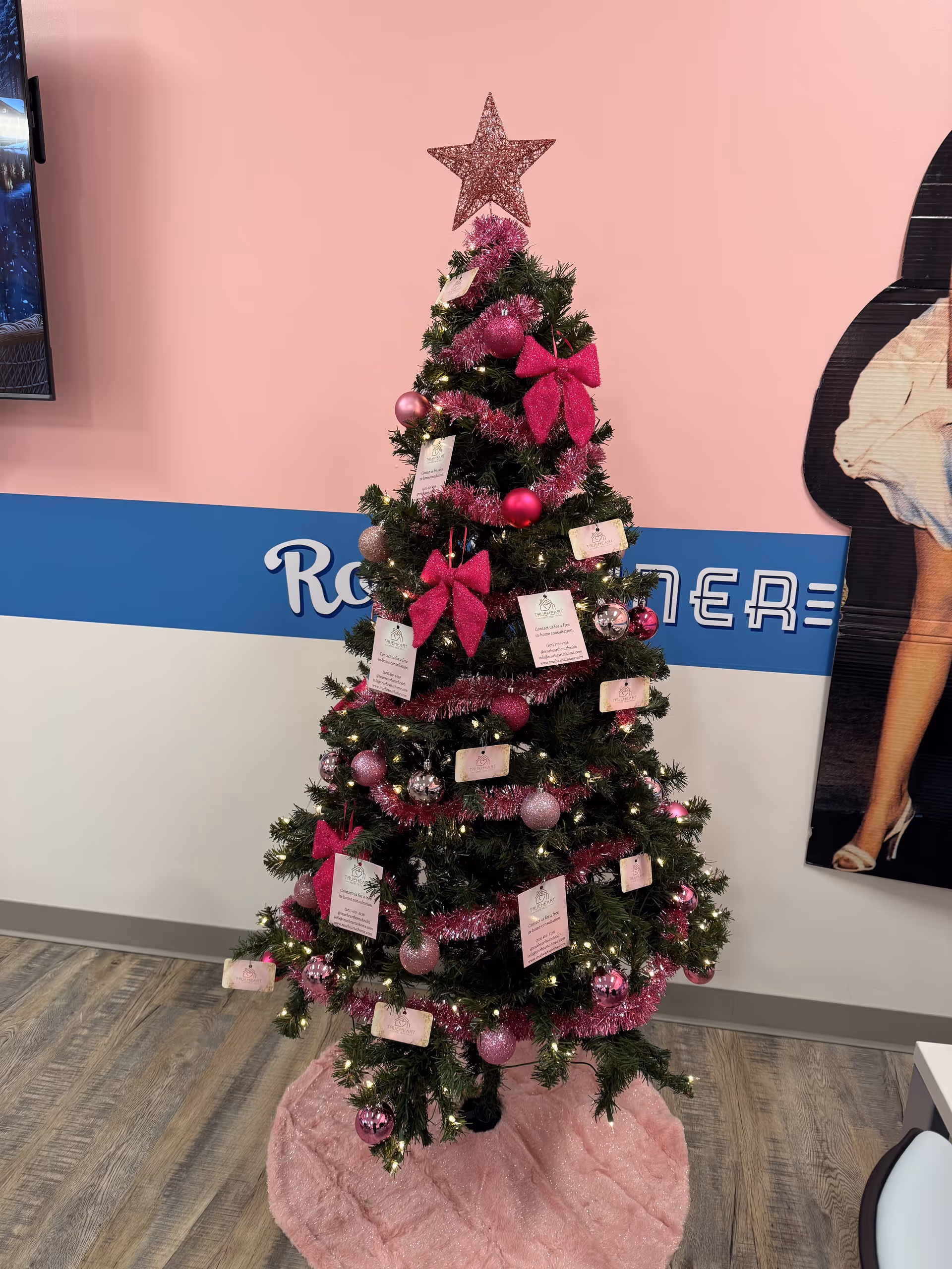 Pink-themed Christmas tree with pink ornaments and ribbons in a facility lobby.