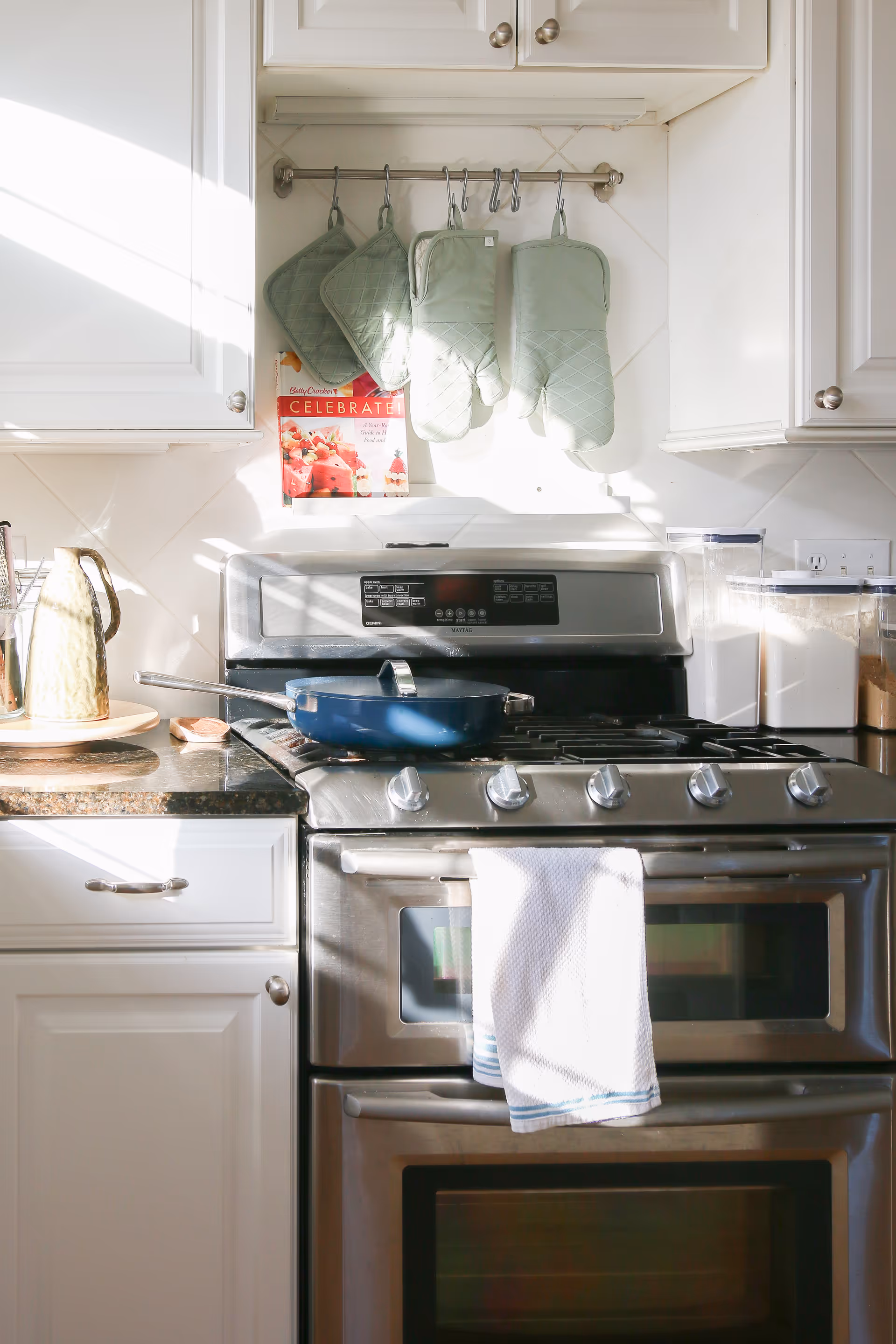 Stainless steel kitchen stove with oven, mitts hanging above, and a towel on the oven handle.
