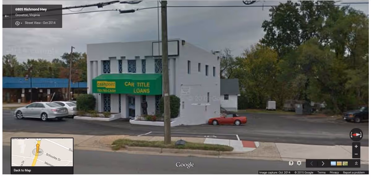 Street view of a white two-story building with a green sign and parked cars.