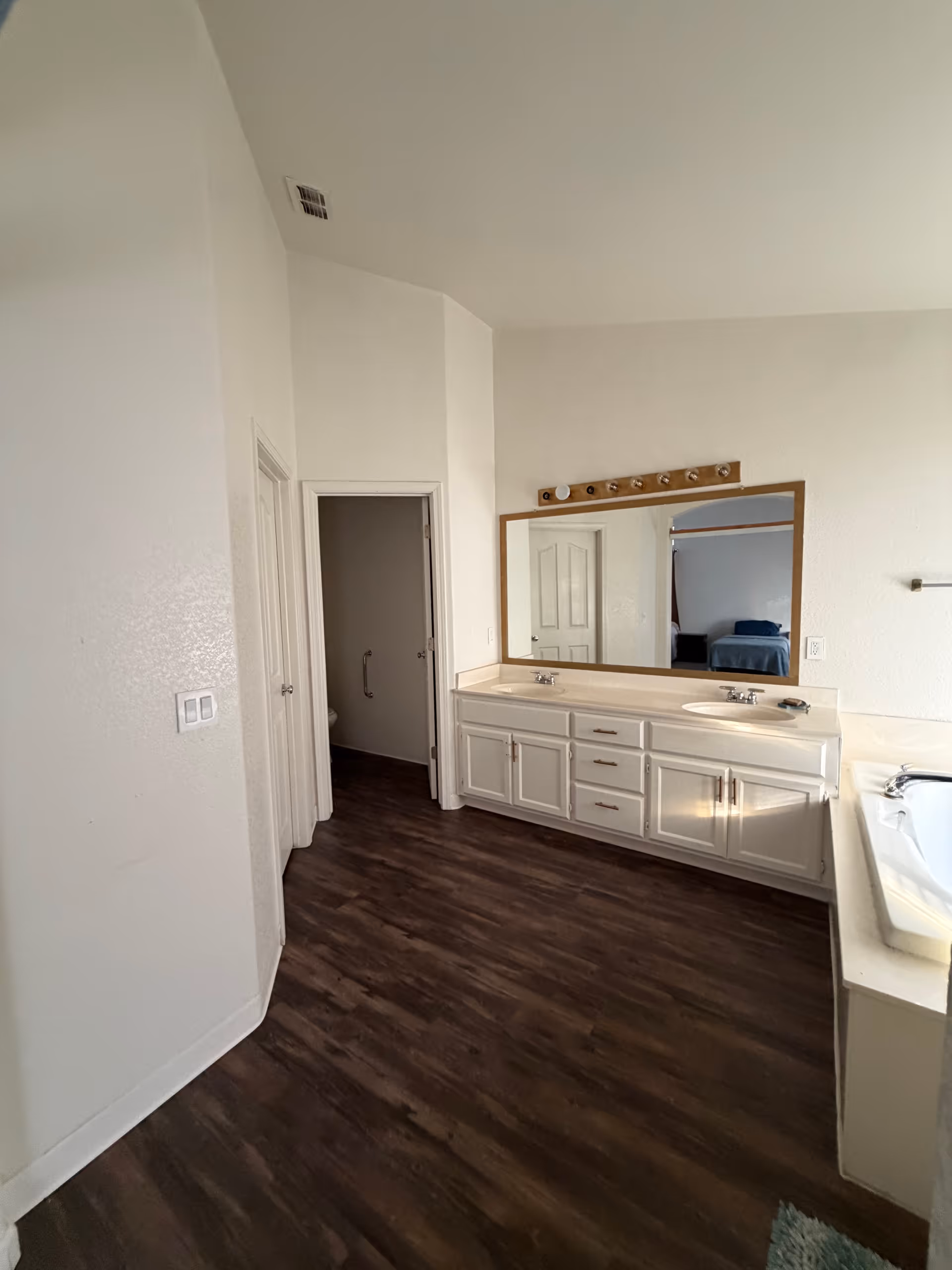 Bathroom vanity with double sinks, large mirror, cabinets, and an open doorway.