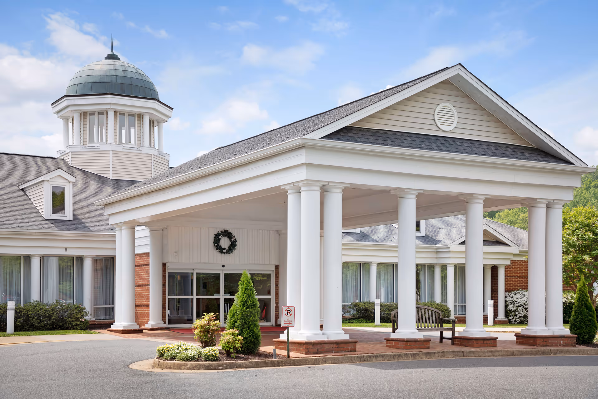 Front exterior of The Colonnades senior living facility with a covered entrance and white columns