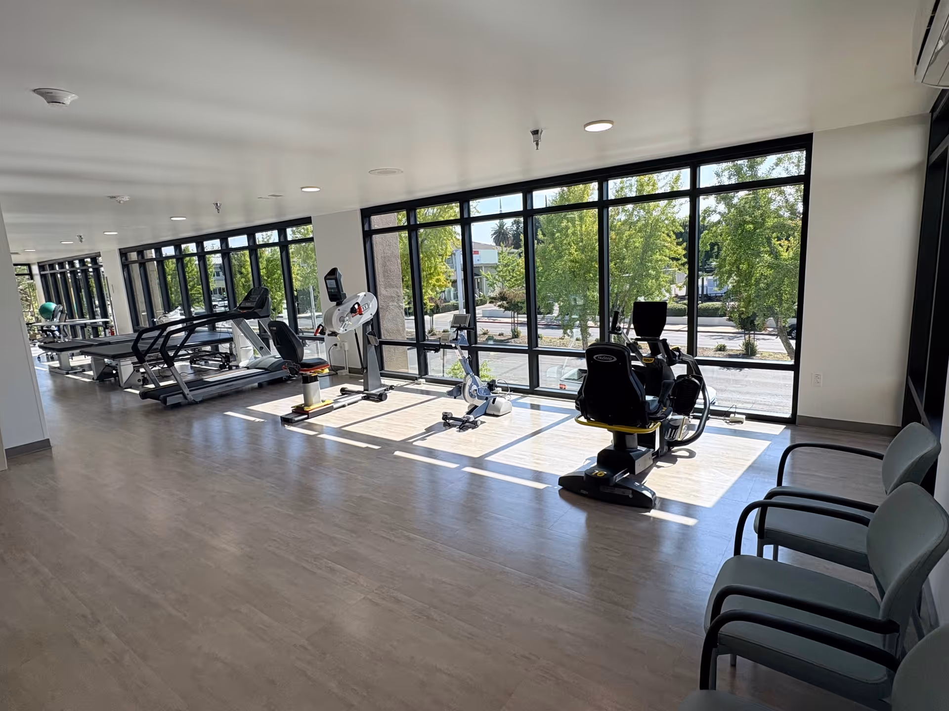 Bright senior fitness center with treadmills and stationary bikes along large windows.