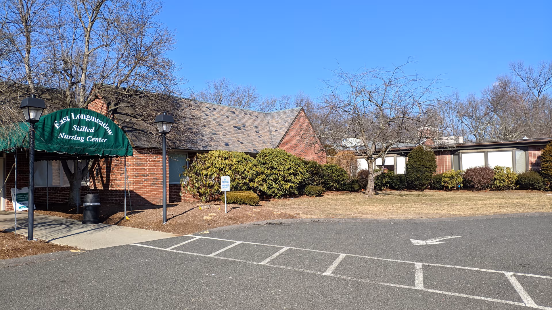 Brick exterior of East Longmeadow Skilled Nursing Center with green canopy entrance and parking