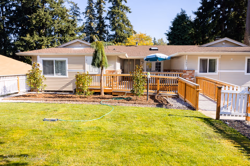 Single-story facility with beige siding, wooden deck, ramp, and a green front lawn.