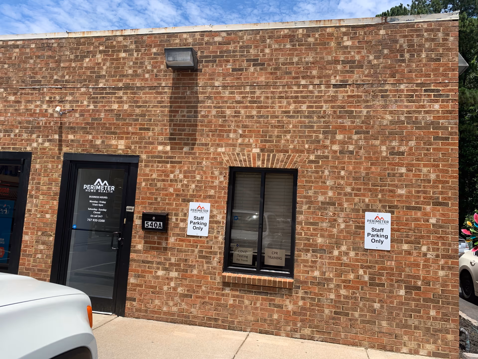Brick exterior of Perimeter Home Health building with door, window, and parking signs.