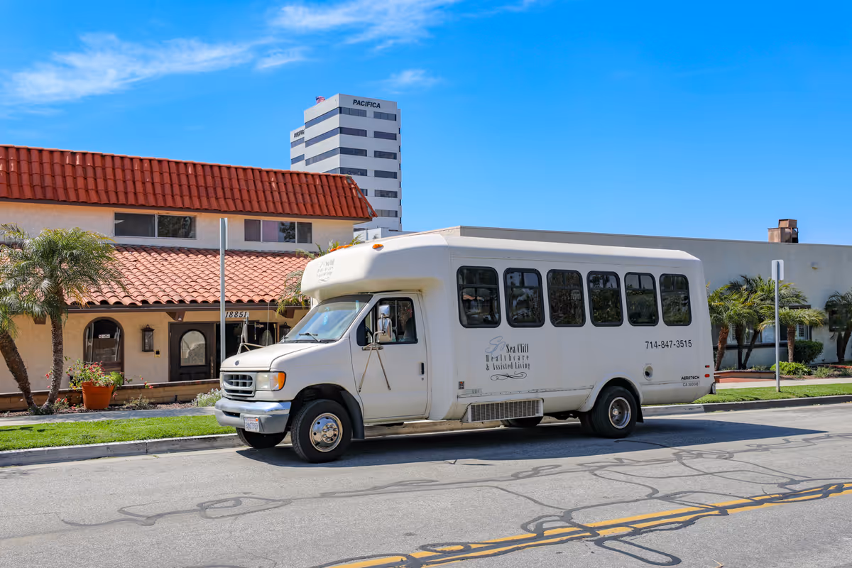White passenger bus parked in front of Sea Cliff Assisted Living building with palm trees.