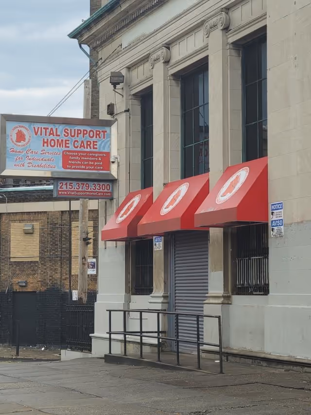 Exterior of Vital Support Home Care storefront with red awnings and signage.