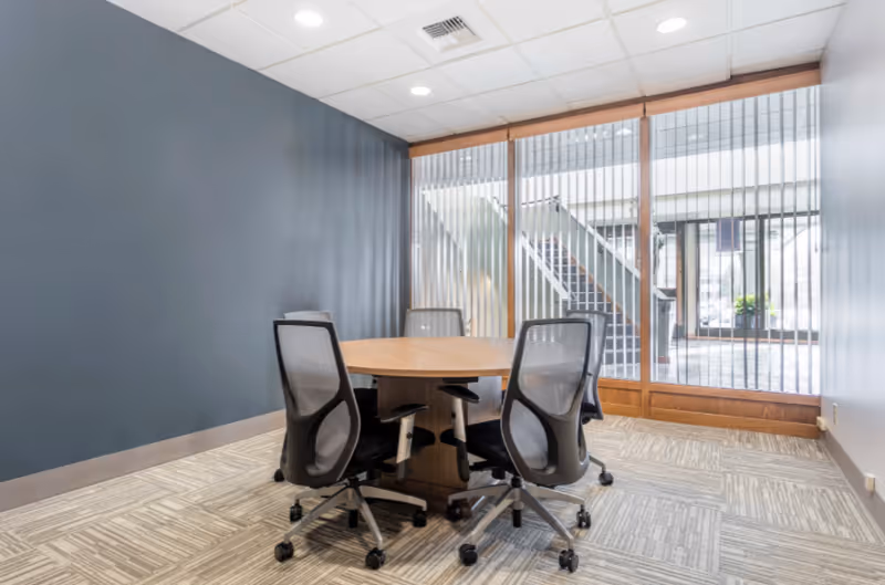 Round wooden table with four mesh chairs in a modern interior meeting room.