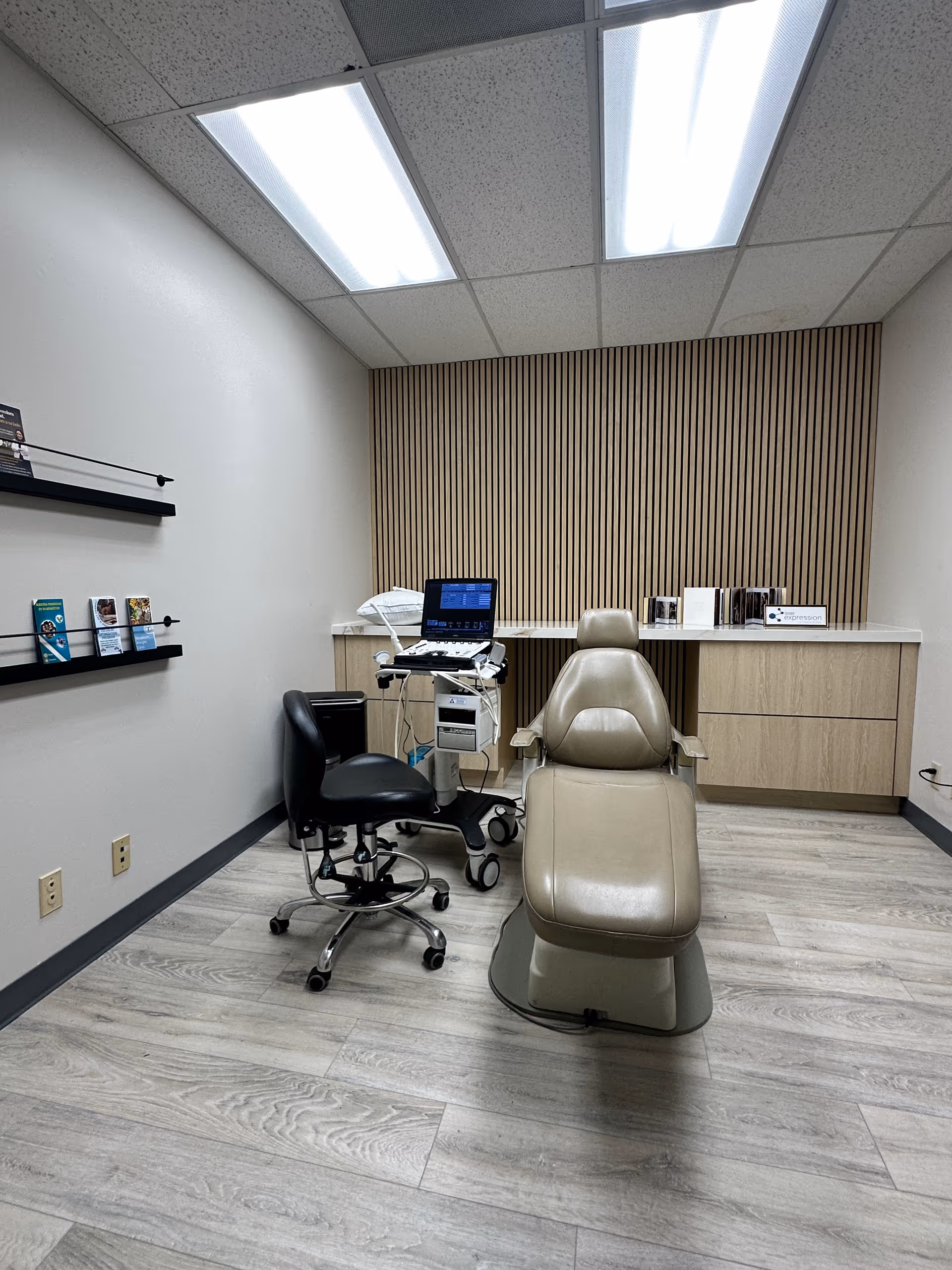 Clinical exam room featuring beige chair, medical equipment, and a wooden wall panel.