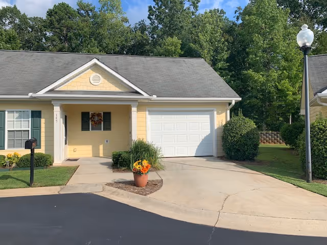 Front view of a yellow senior living facility with a driveway, porch, and attached garage.