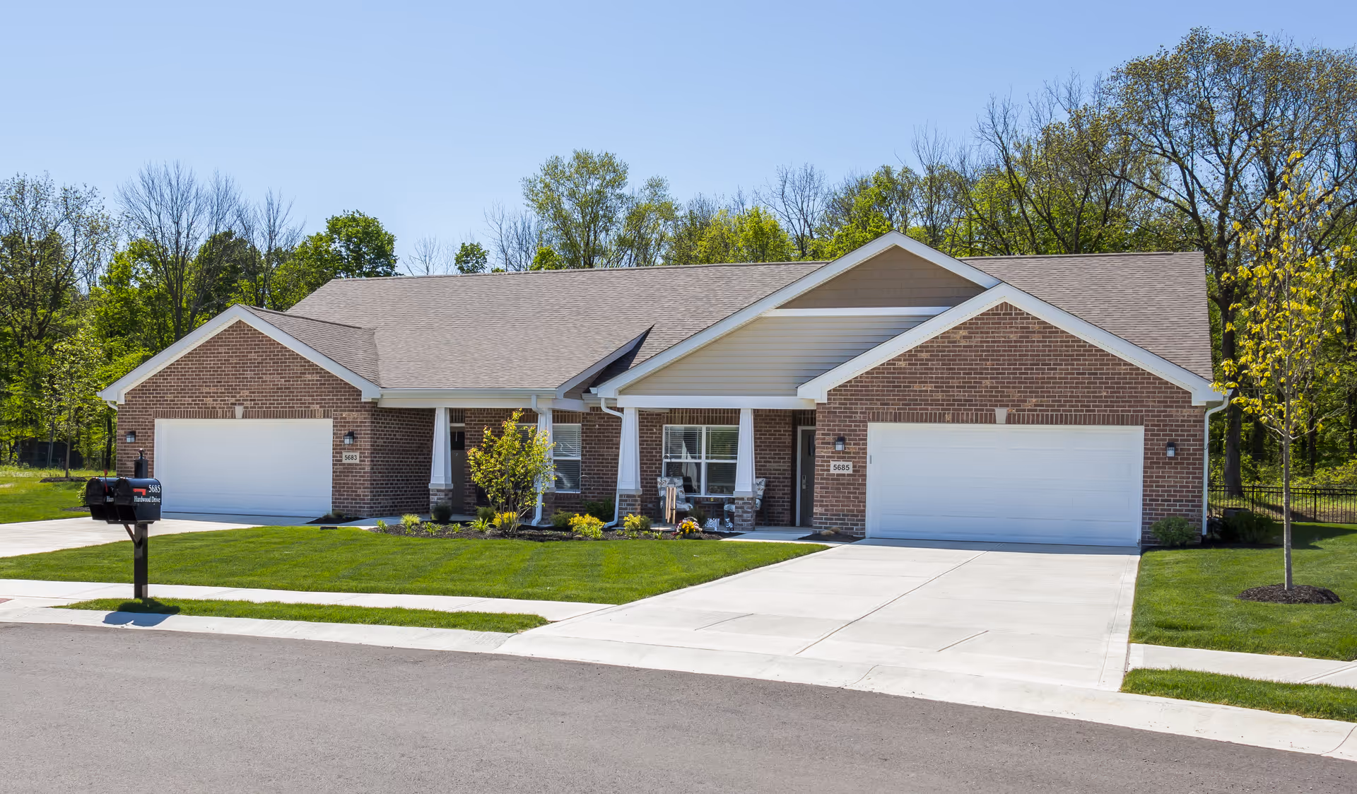 Front exterior of a single-story brick duplex with two garages, driveways, a manicured lawn, and a mailbox.