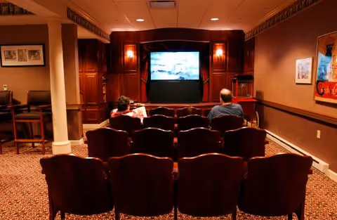 Residents watch a movie in a cozy wood-paneled indoor screening room.