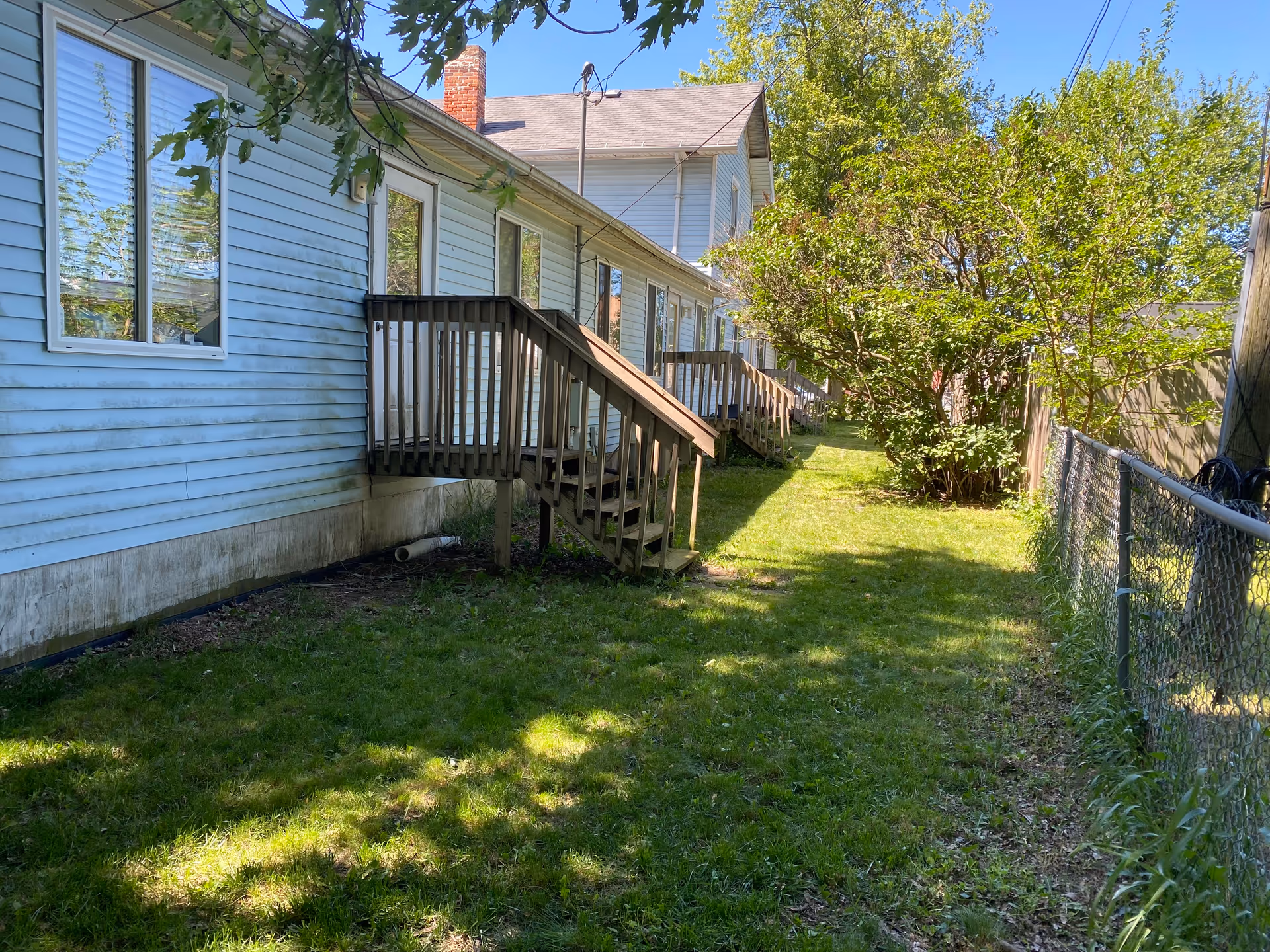 Backyard exterior of a blue senior housing building with wooden stairs, lawn, and chain-link fence.