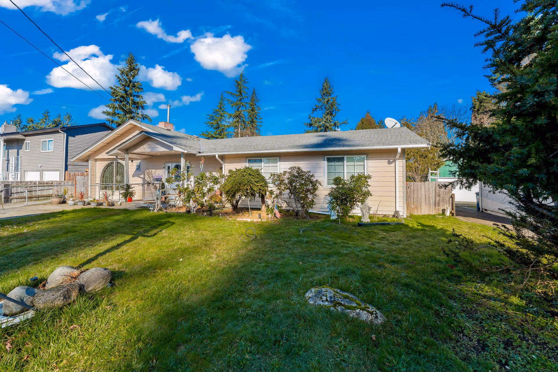 Single-story house with a well-kept front yard and shrubs under a blue sky.