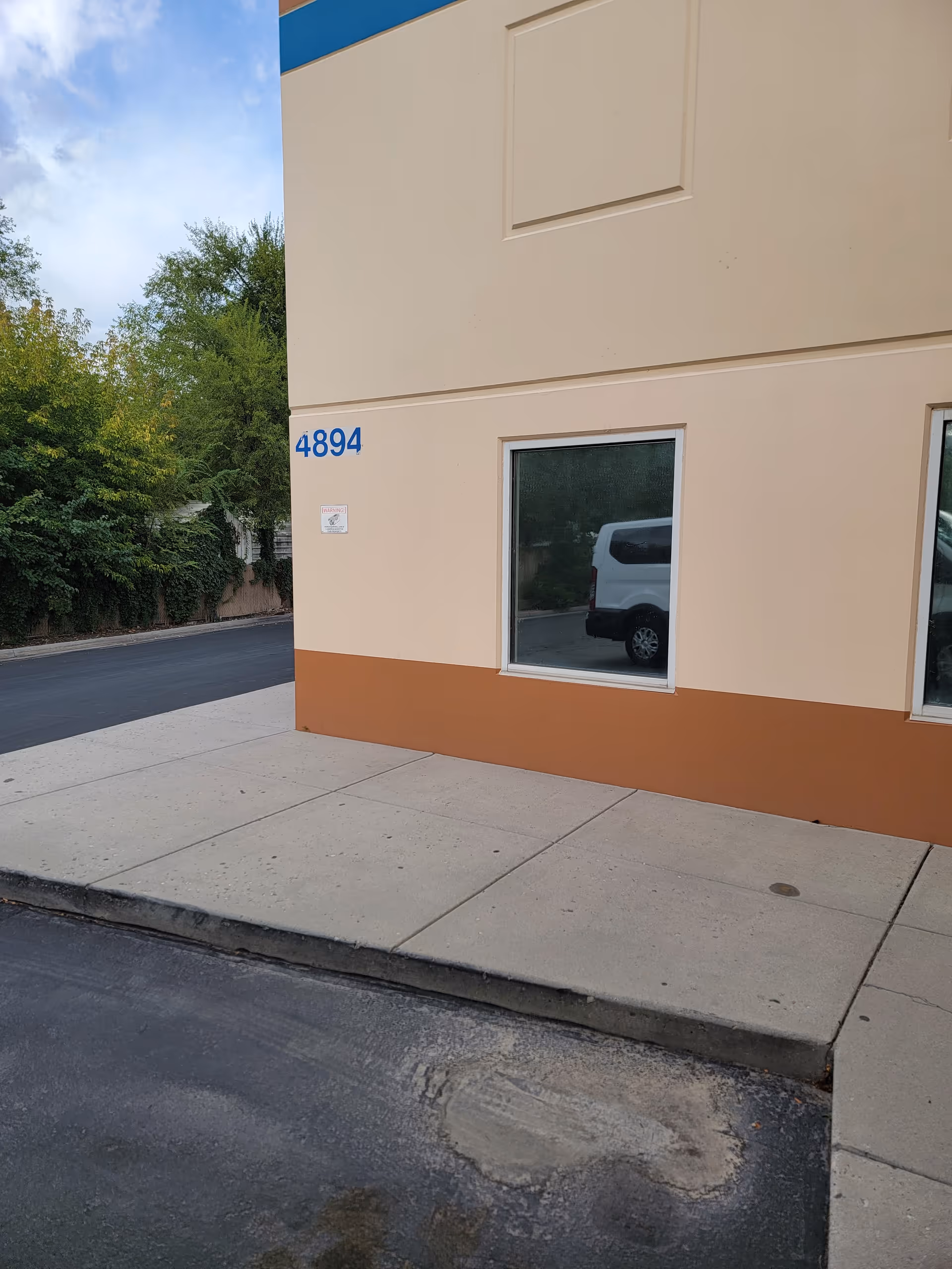 Exterior view of a beige building with blue address numbers and a sidewalk.