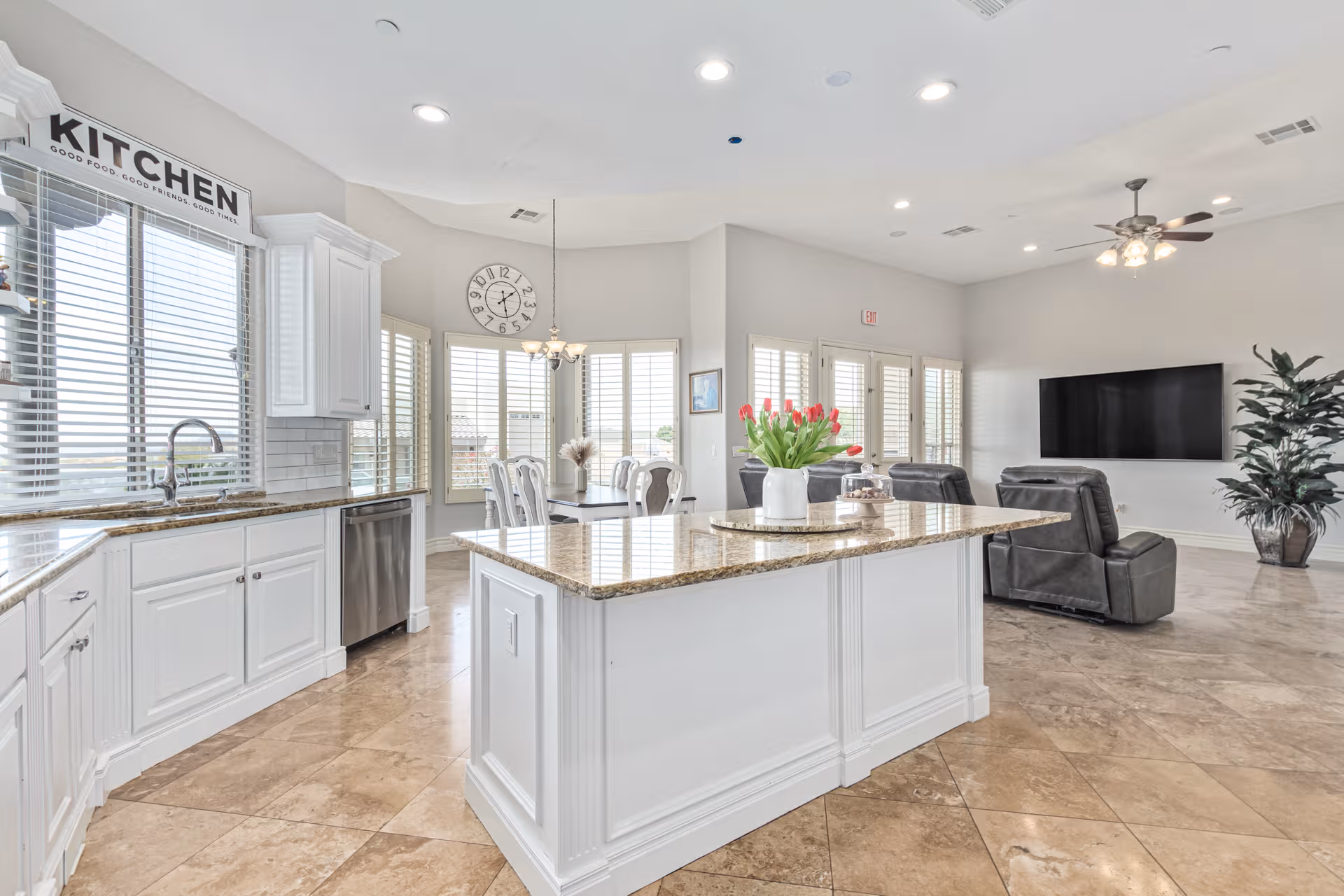 Bright open-plan kitchen and living area with island, white cabinets, granite countertops, and seating.
