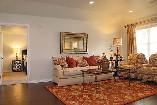 Cozy living room with beige sofa, red cushions, patterned chairs, and a coffee table.