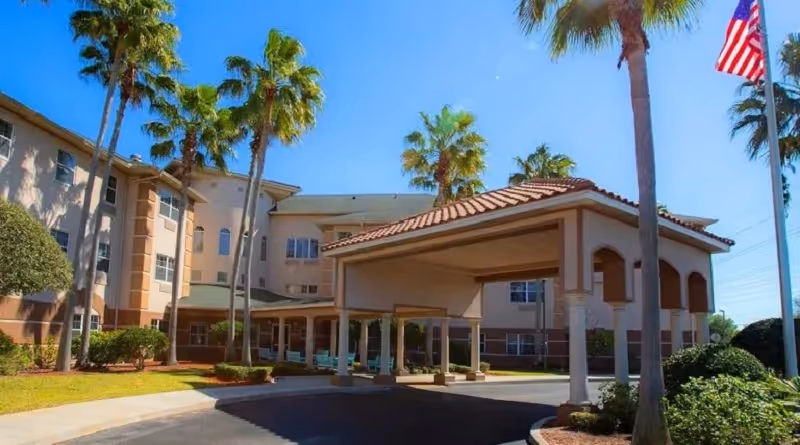 Outdoor view of Hibiscus Court senior living facility with palm trees and a covered entrance.
