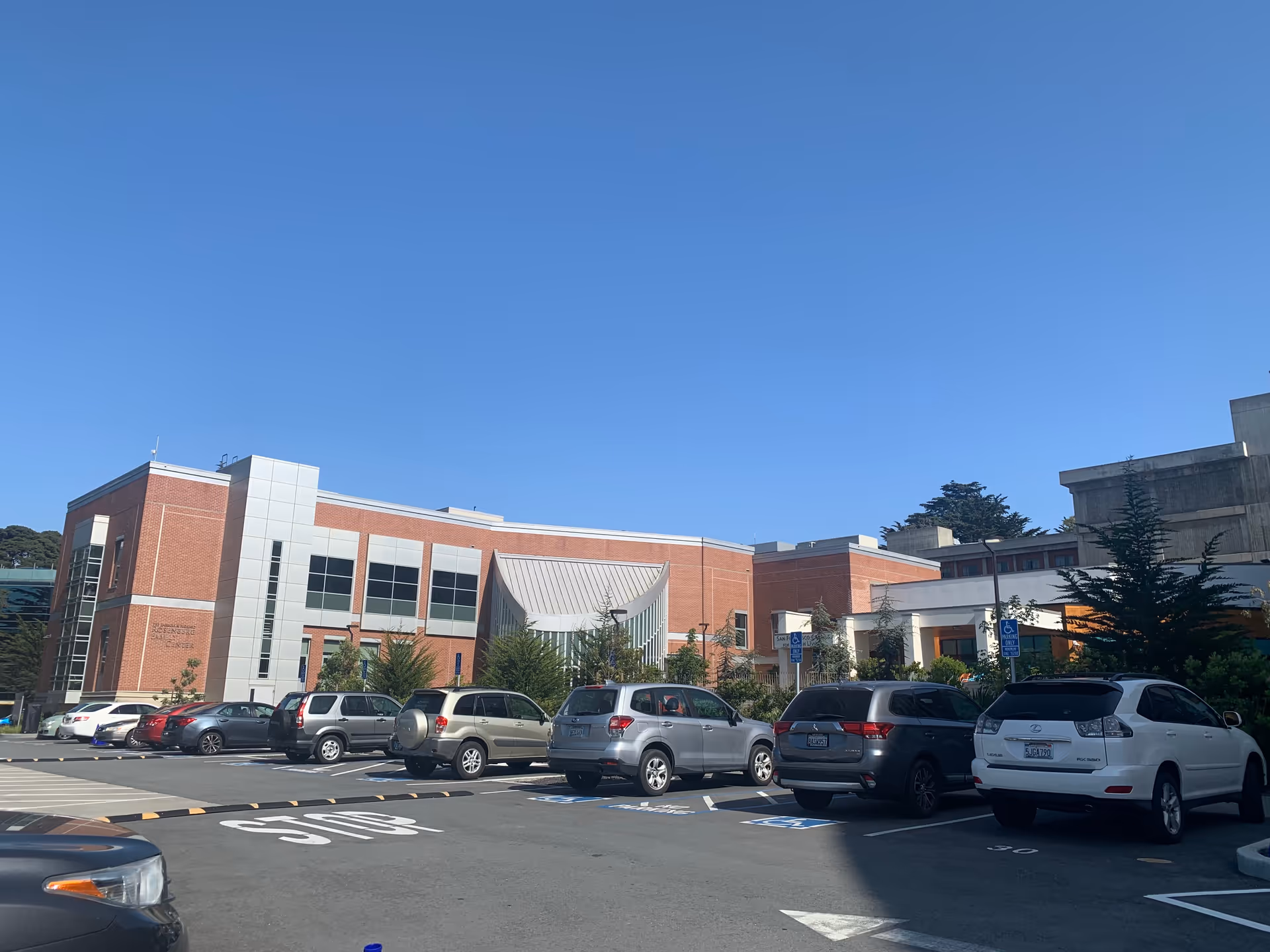Exterior view of a brick campus building with a parking lot and clear blue sky.