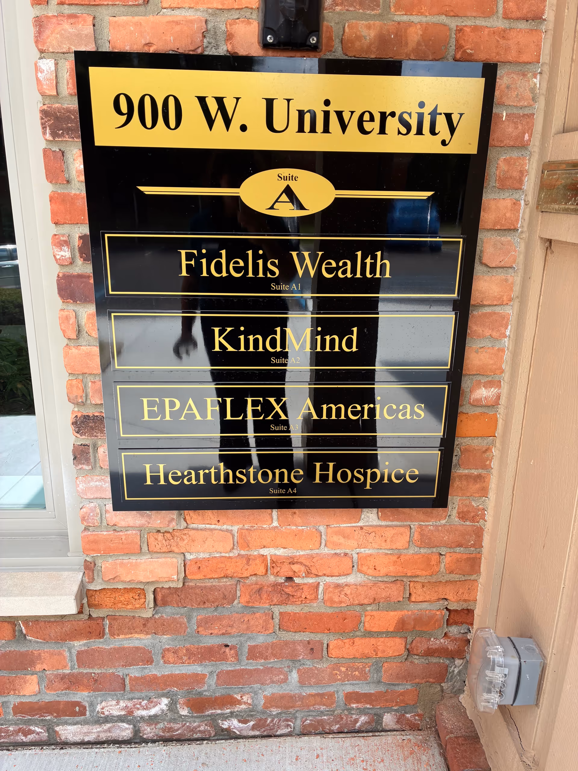 Brick building exterior with a signboard listing suites including Hearthstone Hospice and 900 W. University.