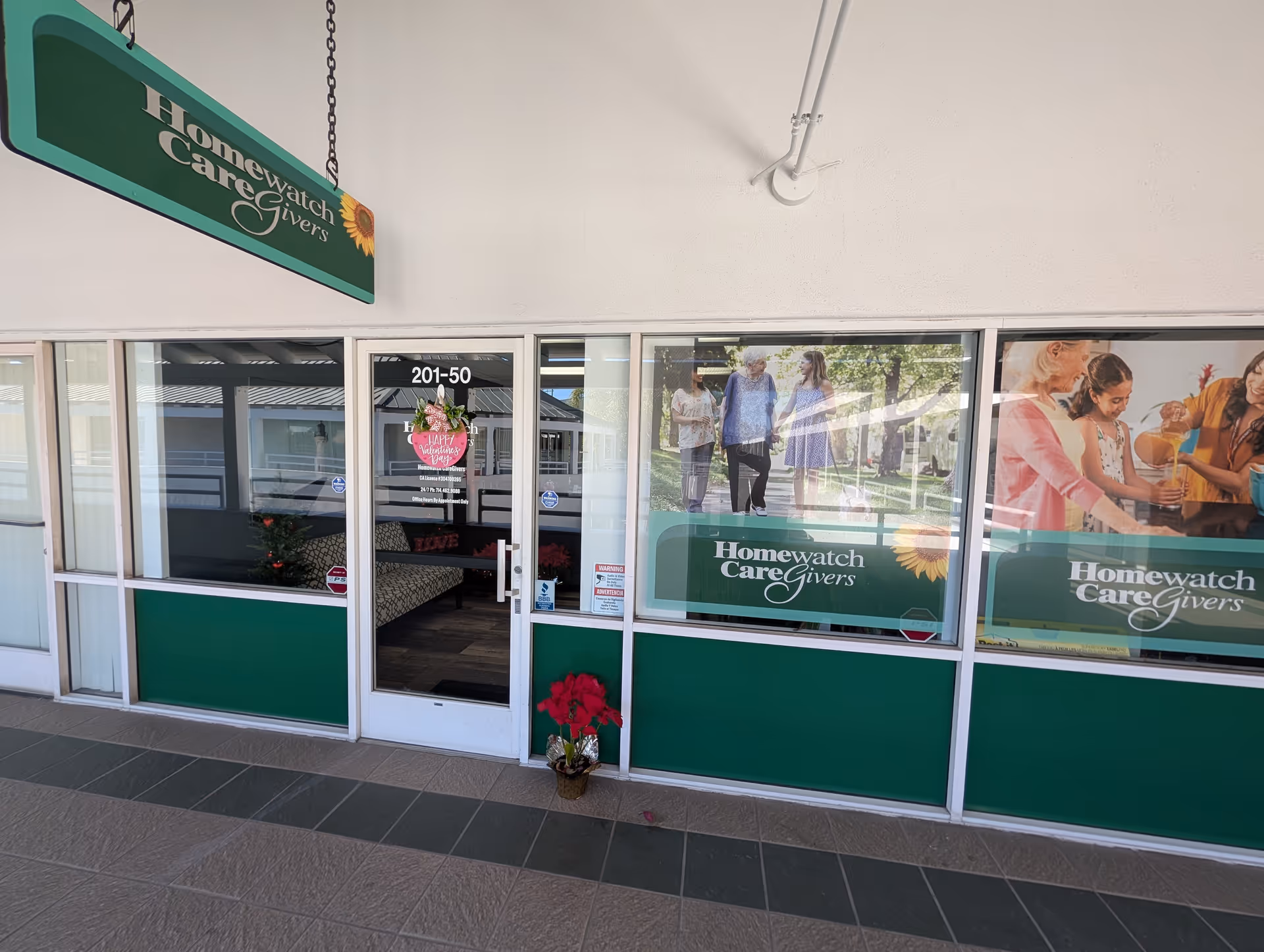 Front view of a storefront showing Homewatch CareGivers signage and glass doors with potted flowers.