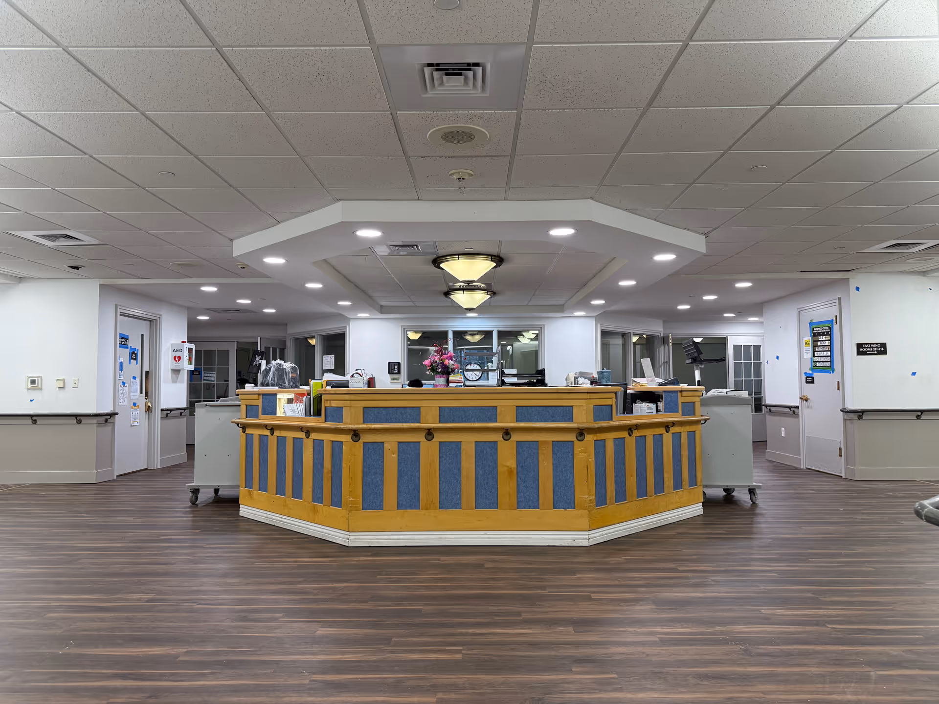 Central reception desk in a senior living facility lobby with wood floors and overhead lighting.
