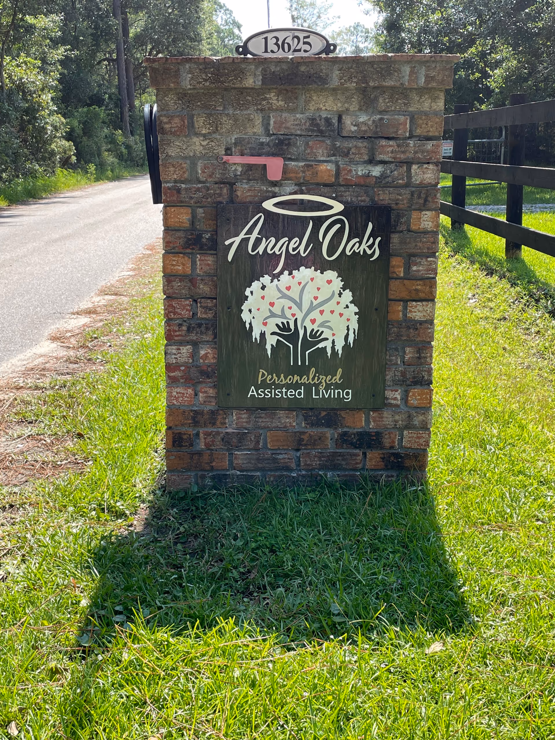 Brick pillar with Angel Oaks sign beside a grassy road and pink mailbox