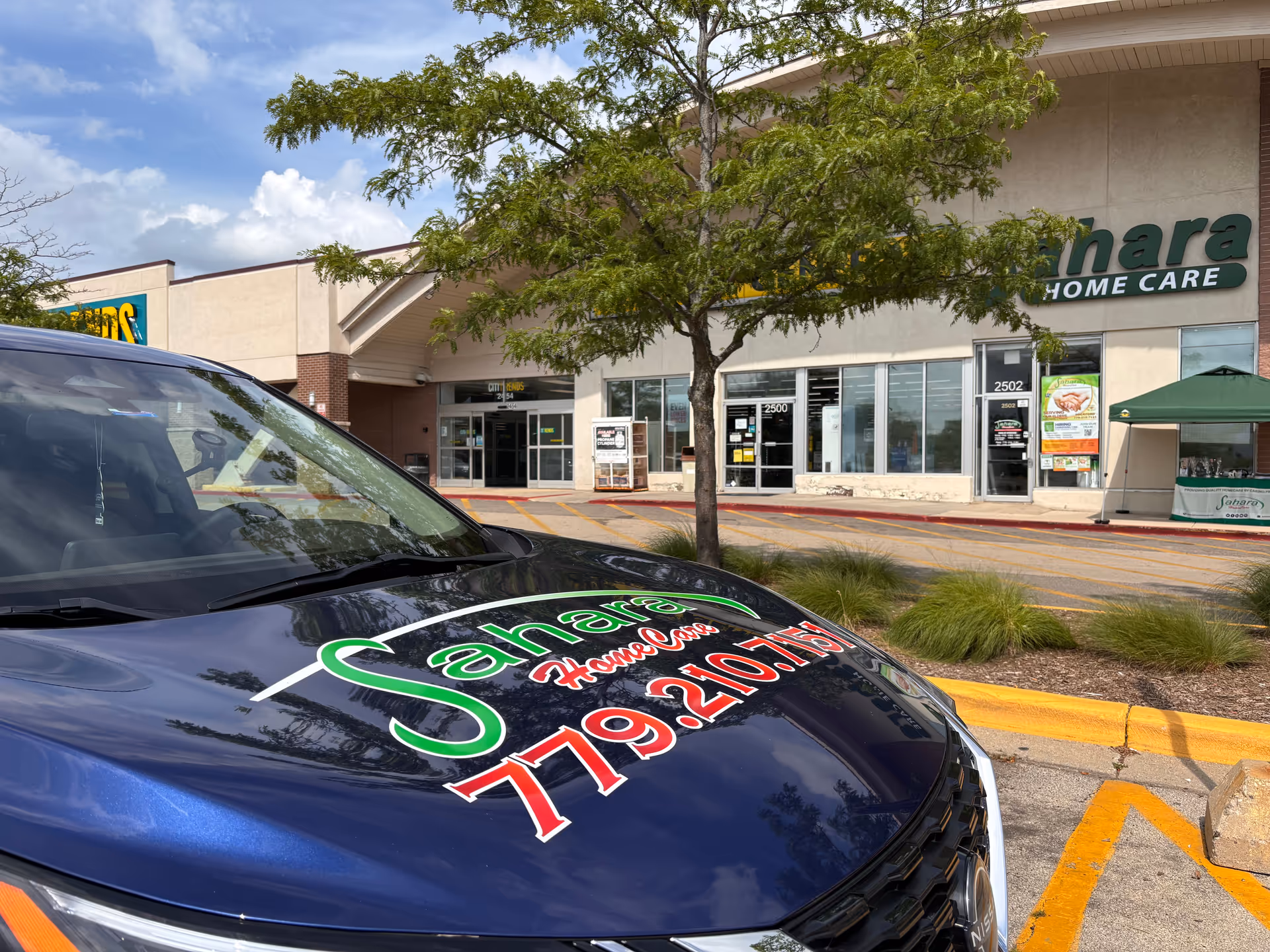 Exterior view of Sahara Home Care storefront with a branded SUV in the parking lot.