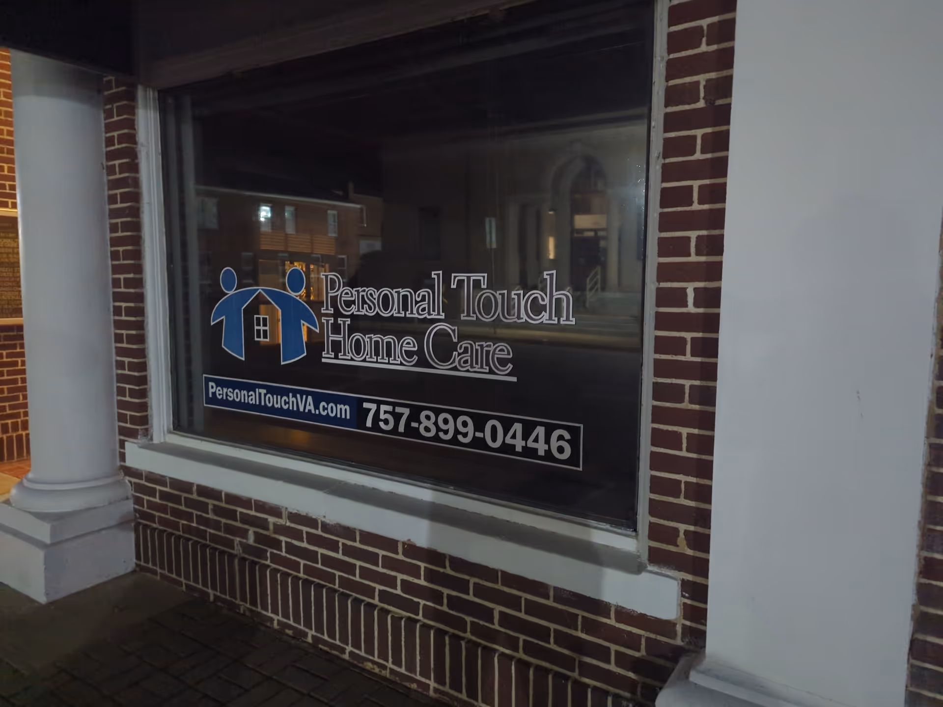 Exterior brick storefront window showing Personal Touch Home Care sign and phone number.