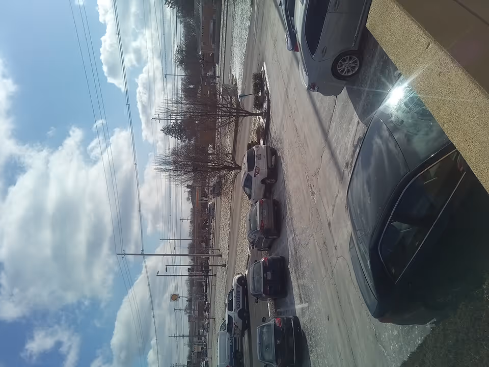Outdoor street scene with parked cars and power lines under a blue sky.