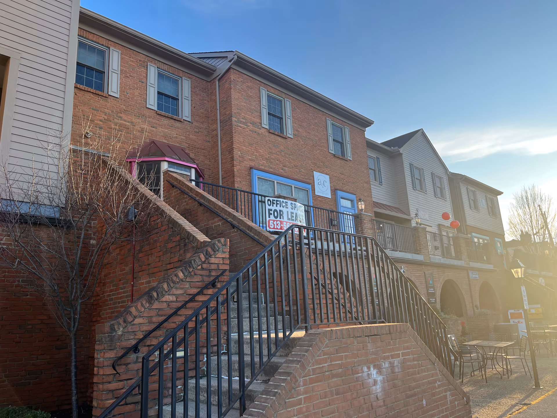 Brick multi-story building exterior with stairs, metal railing, and a for-lease sign.