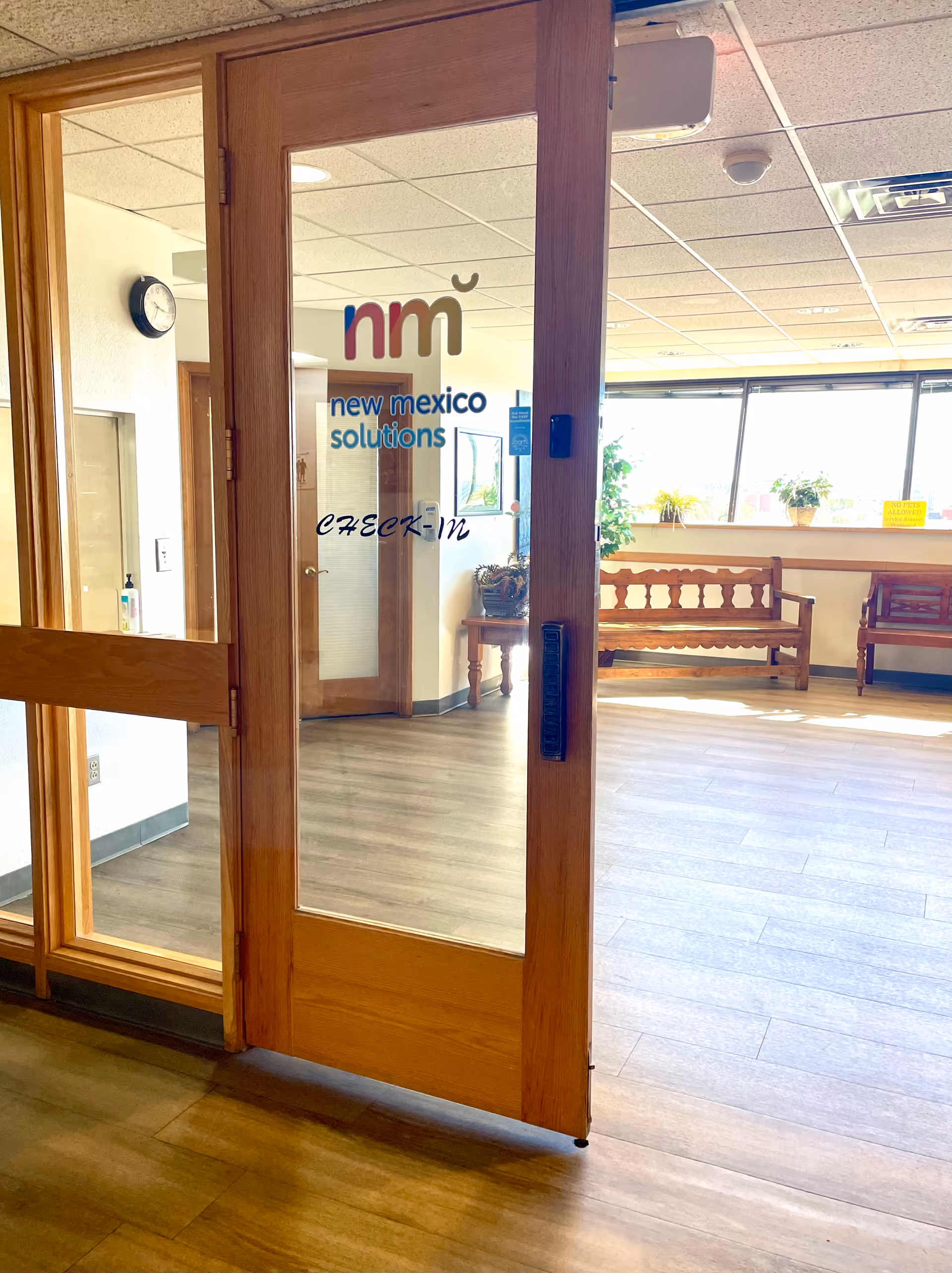 Glass entry door with New Mexico Solutions branding opens to a bright lobby with benches.