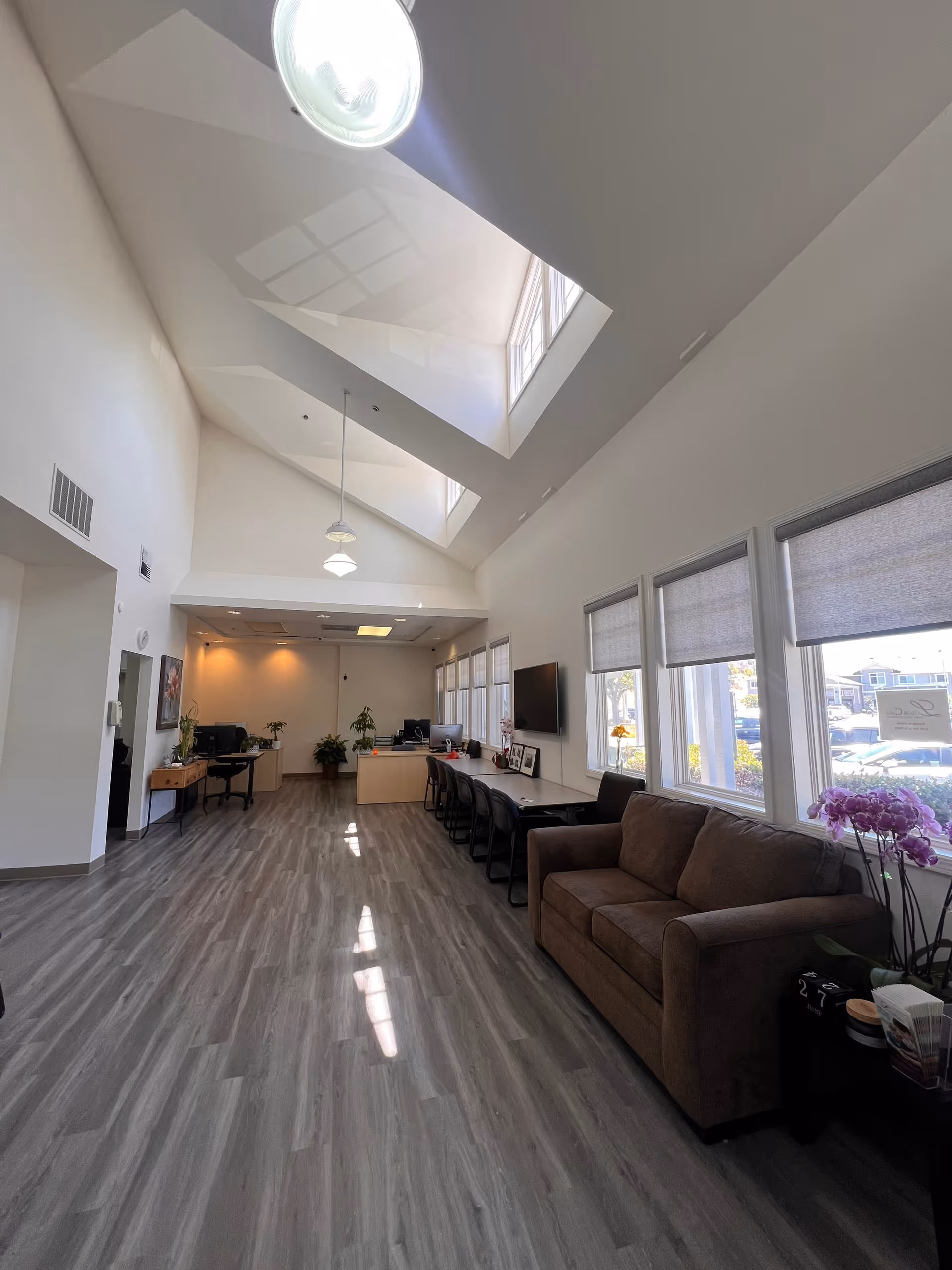 Bright, airy reception area with skylights, a long desk, chairs, and a brown sofa.