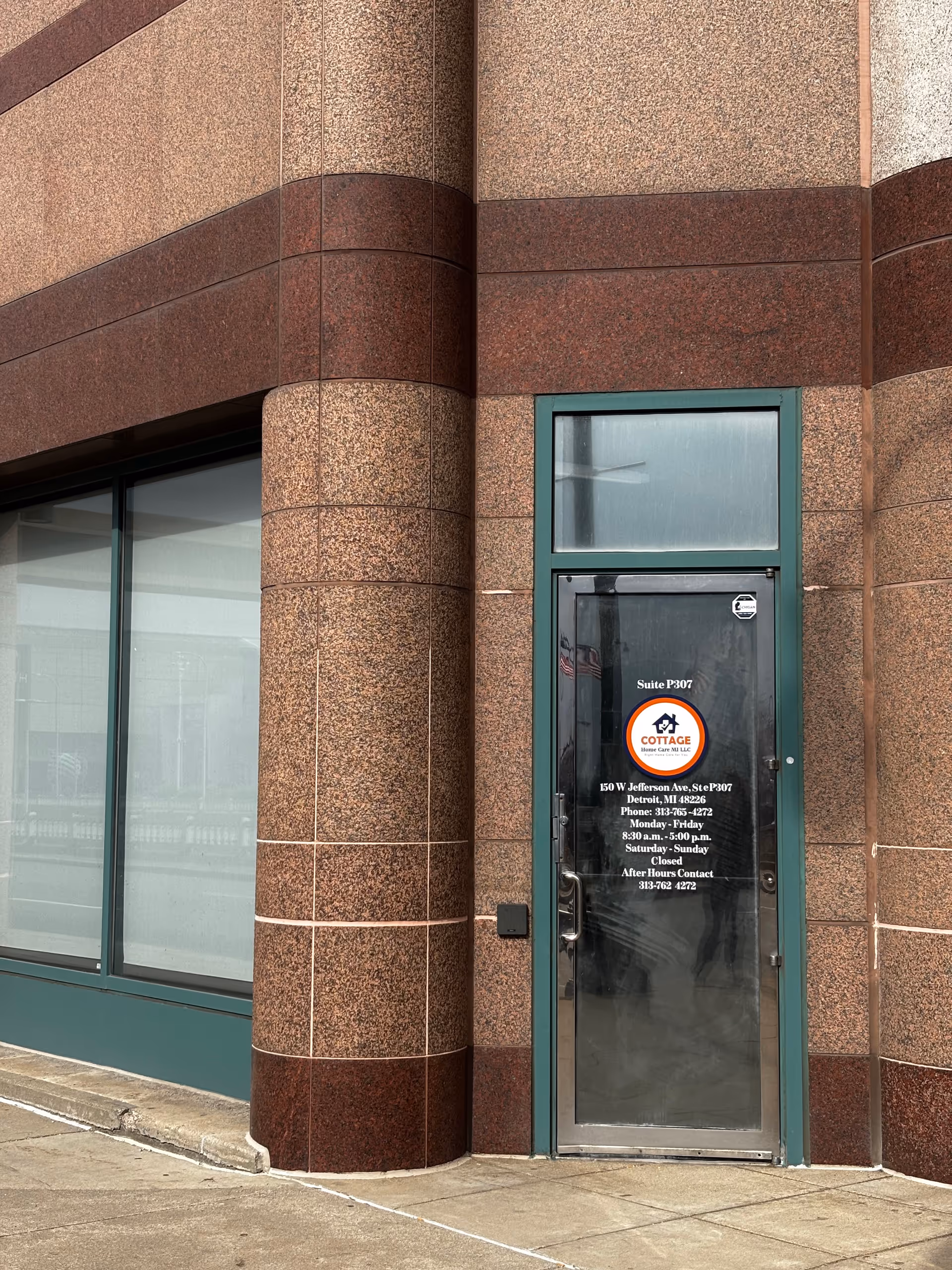 Exterior view of a building entrance with teal-framed glass door and brown stone facade.