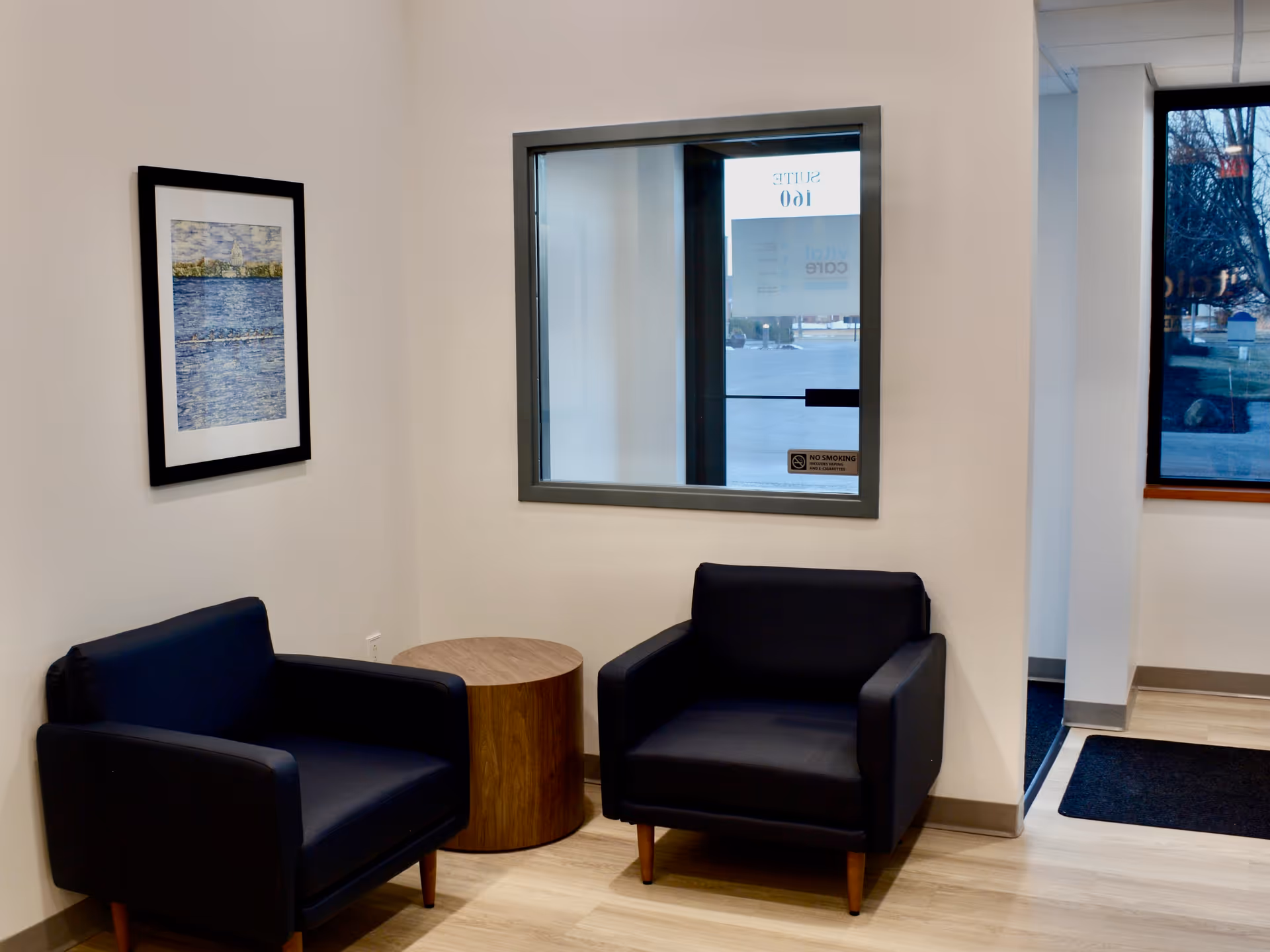 Two dark blue armchairs flank a round wooden table in a small beige waiting area.