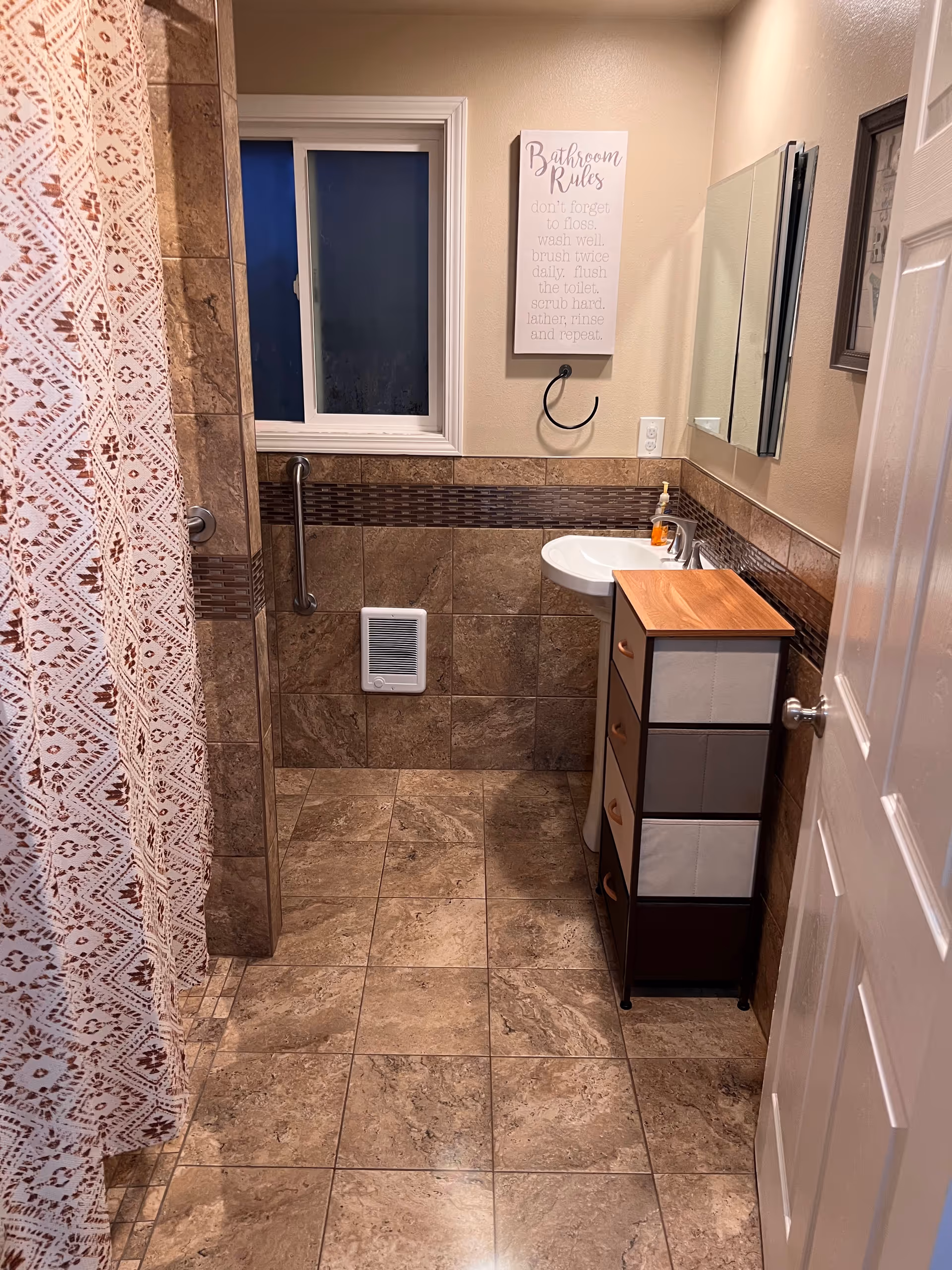 Bathroom with tiled walls, a shower curtain, sink, and 'Bathroom Rules' sign above mirror.