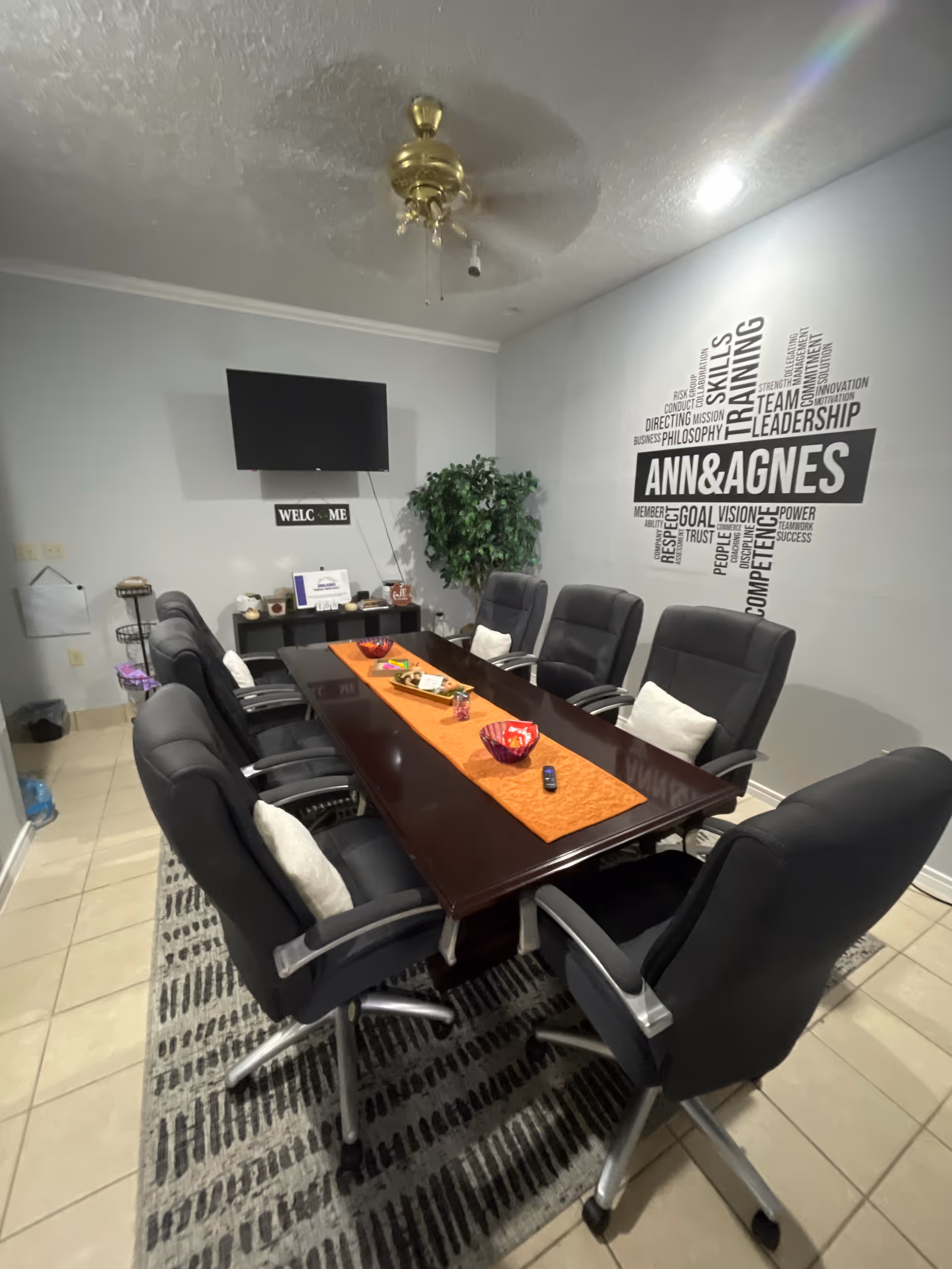 Conference room with a long wooden table, black chairs, ceiling fan, and ANN&AGNES wall logo.