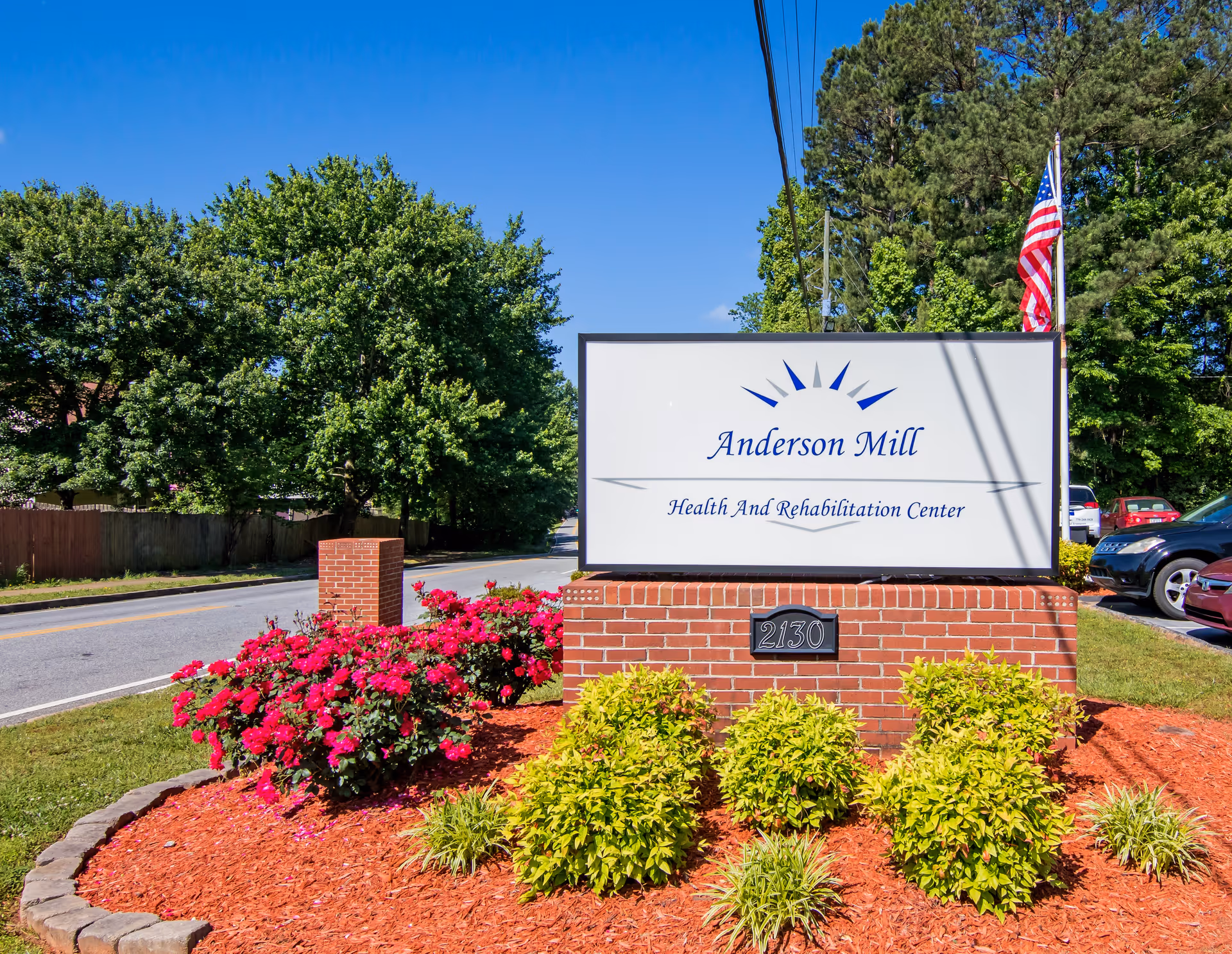 A white sign reads Anderson Mill Health and Rehabilitation Center, surrounded by red mulch and flowers.