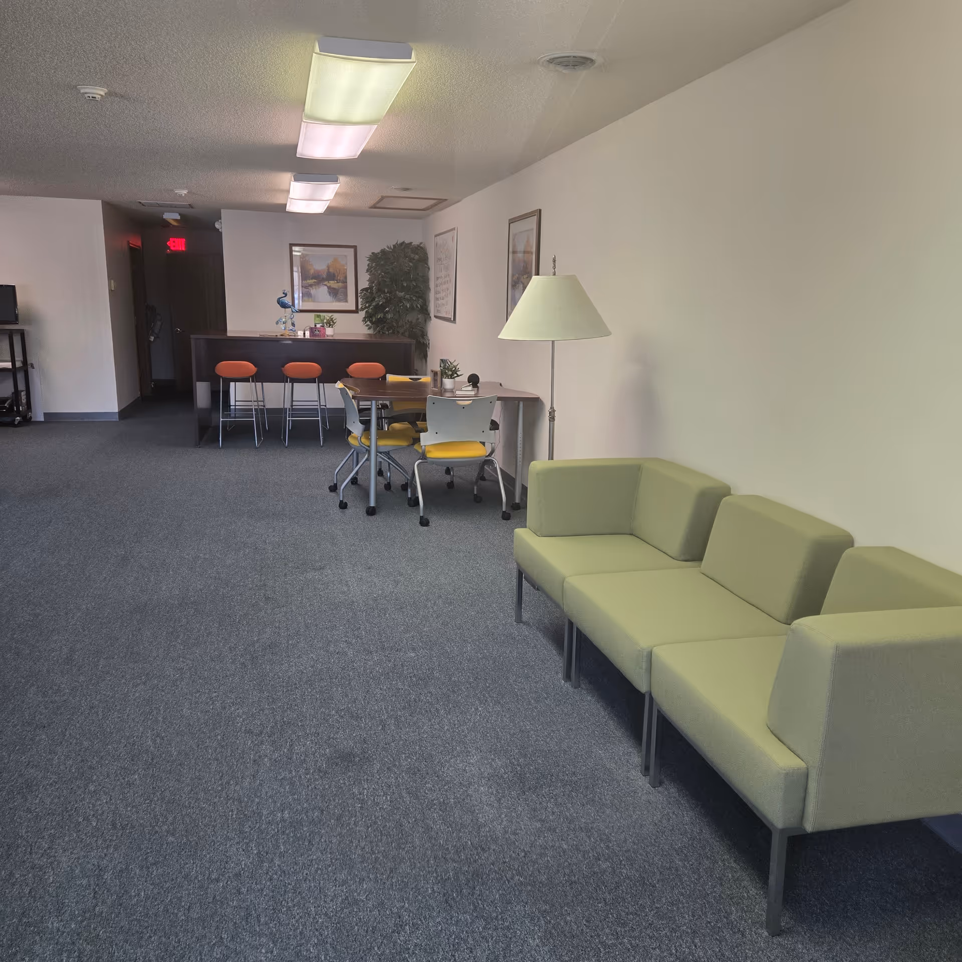 A quiet senior living lounge with lime-green seating, a table, and bar stools.