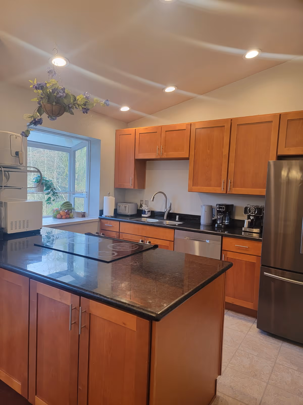 Bright kitchen with wooden cabinets, granite island, stainless appliances, and a window.