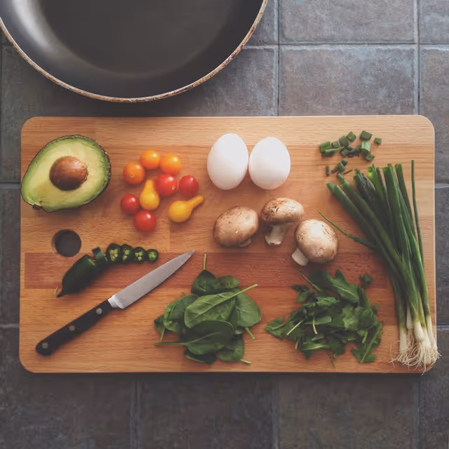 Top-down view of fresh vegetables and a knife arranged on a wooden cutting board.