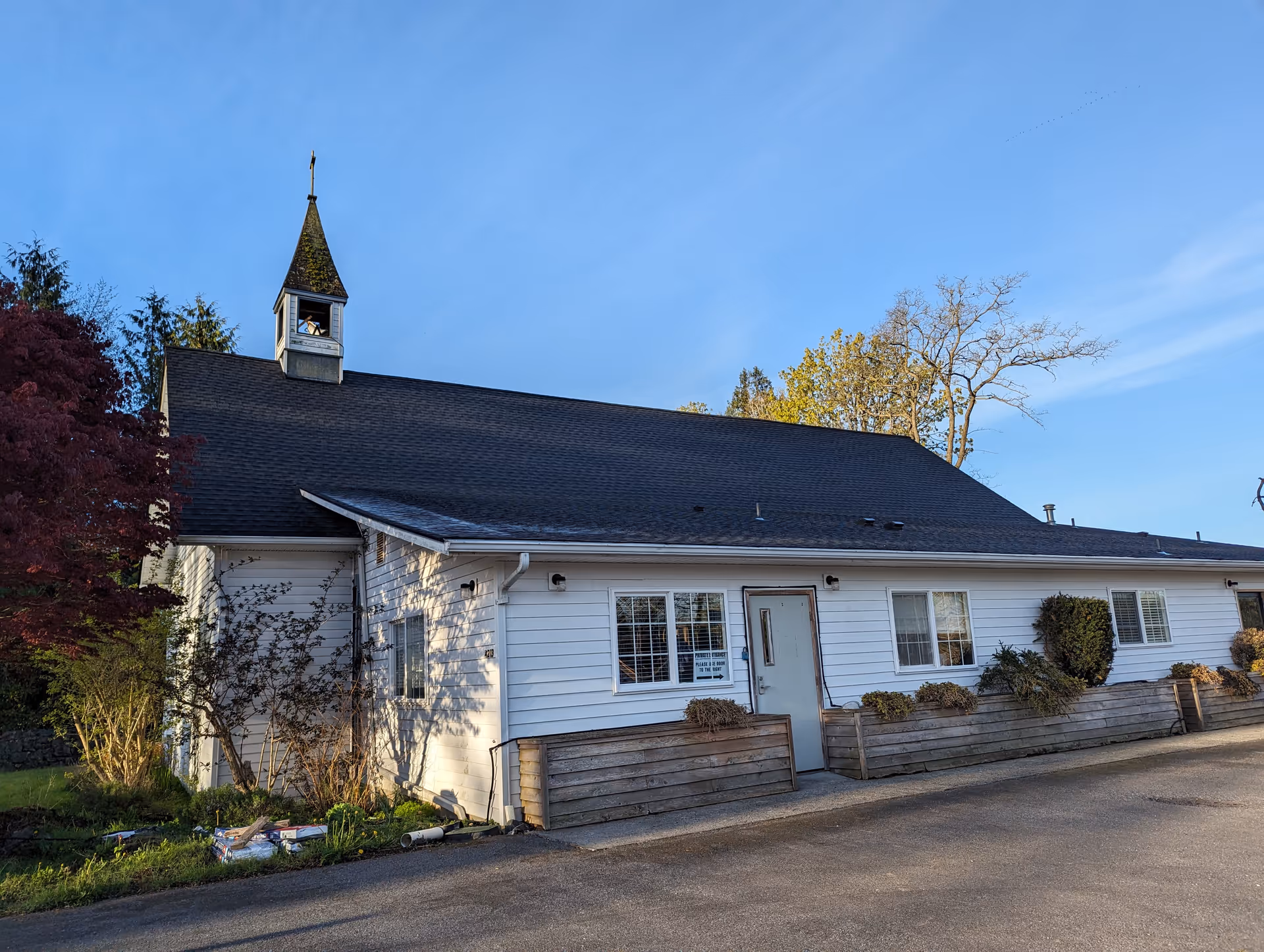 White single-story building with a small steeple, front planters, and trees.