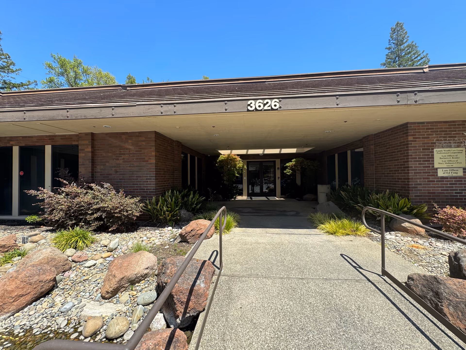 Brick senior living facility entrance with a covered walkway and landscaped rocks and plants.