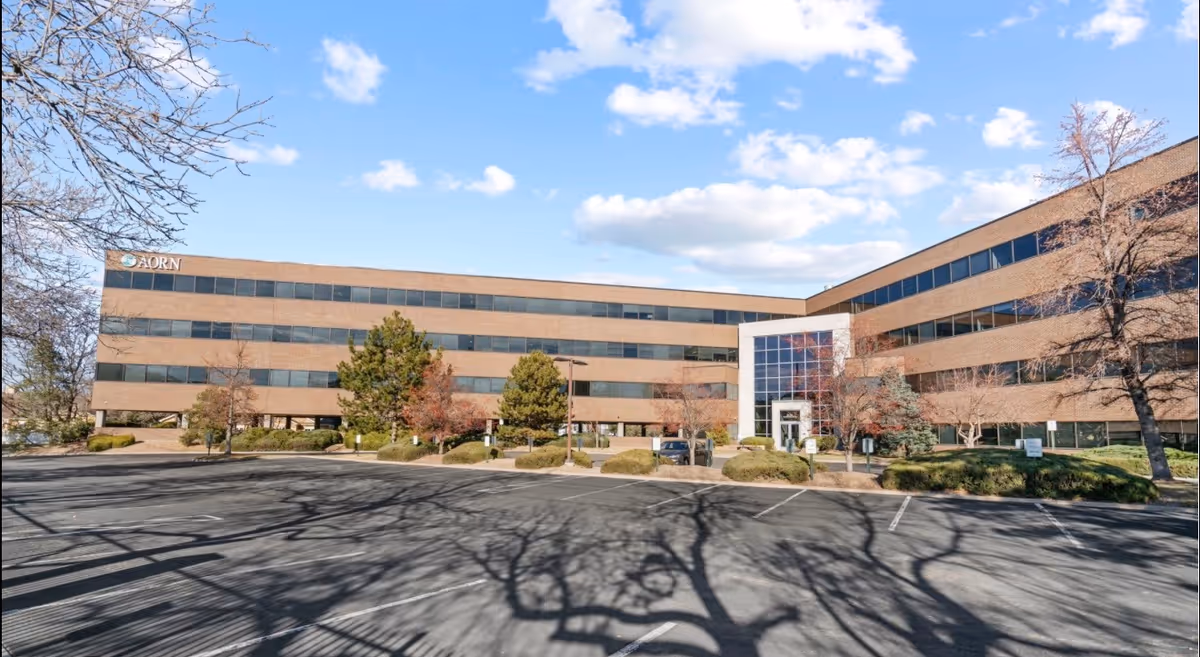 Exterior view of a large brick building with a glass entrance and parking