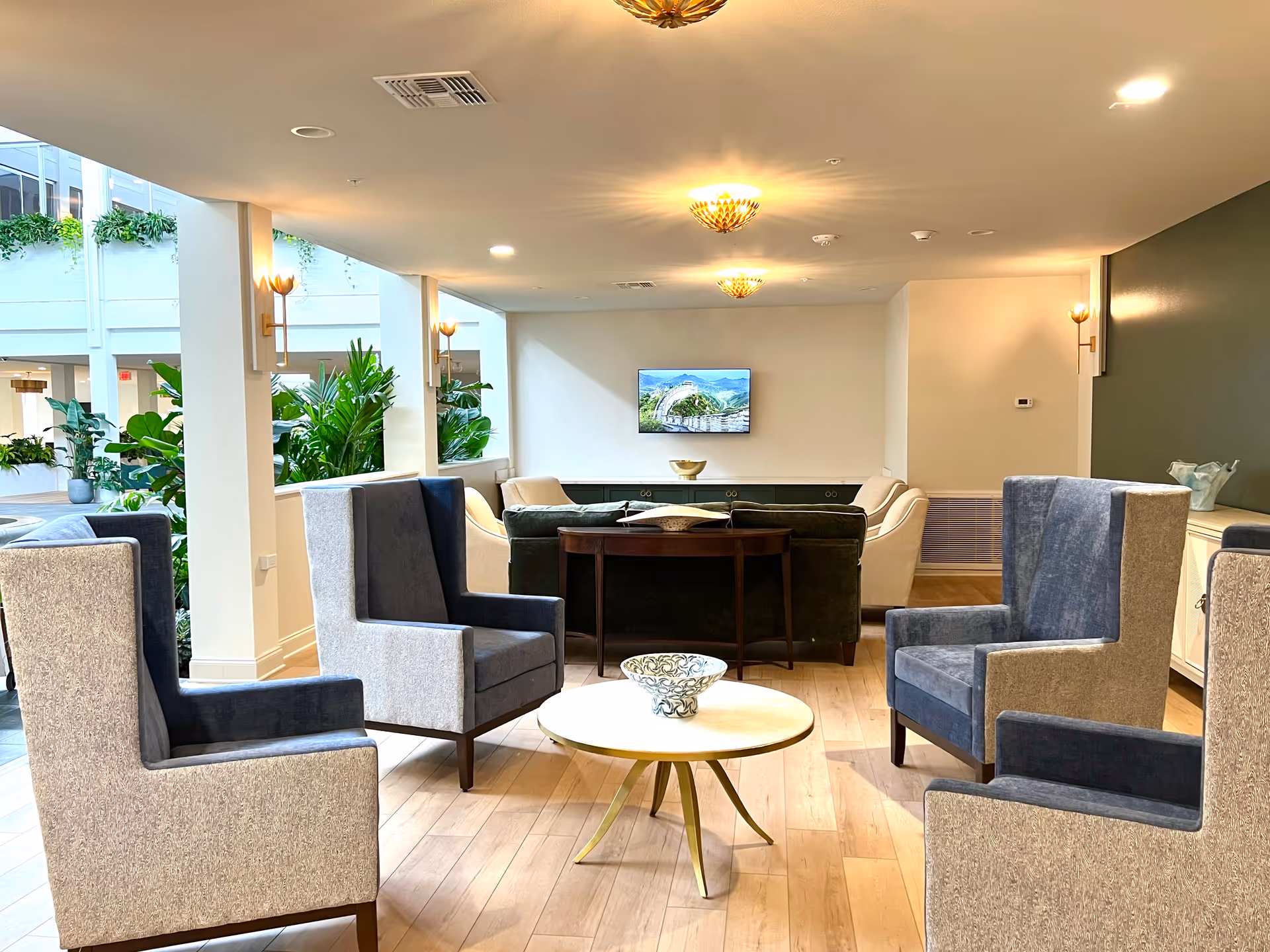 Bright senior living lounge with blue chairs, a round table, and a wall-mounted TV.