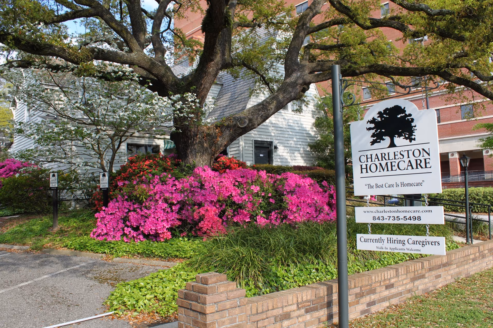 Front of Charleston Homecare facility with a large sign, flowering shrubs, and a tree.