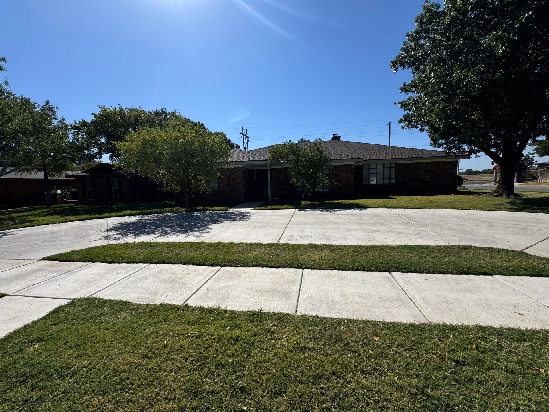 Single-story brick facility with landscaped lawn, sidewalks, and trees under a sunny blue sky.